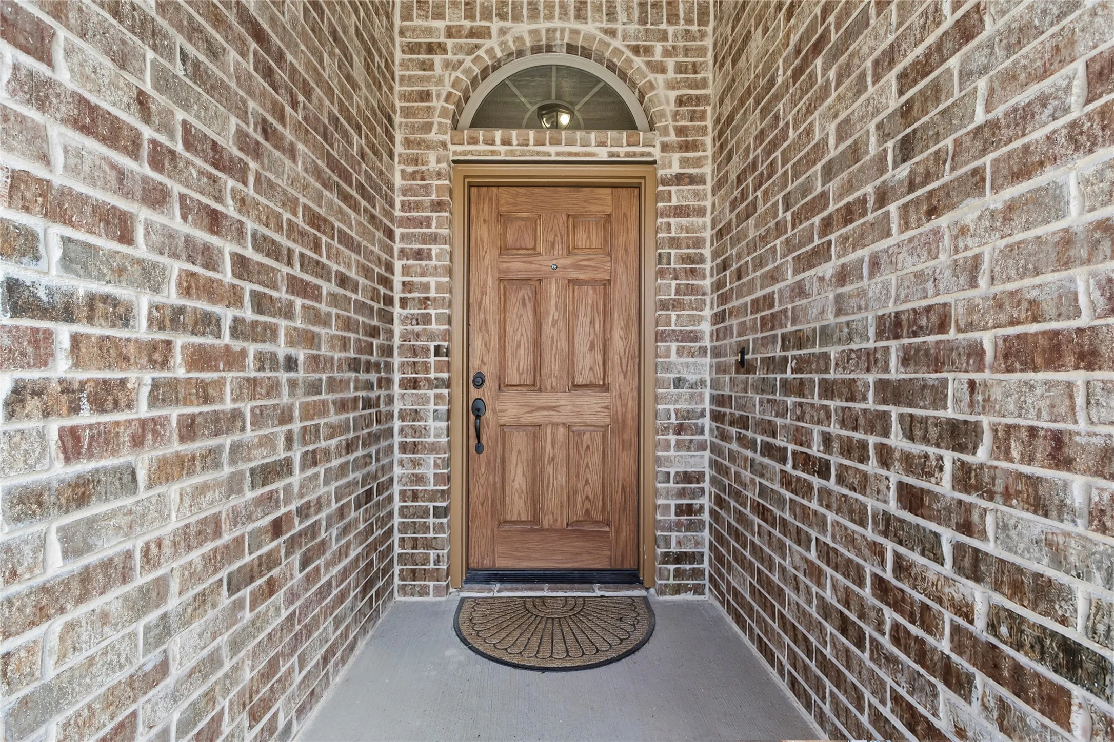 Inviting front entry featuring a paneled wood-finish door with an arched transom window, set within multi-toned brickwork and a concrete porch