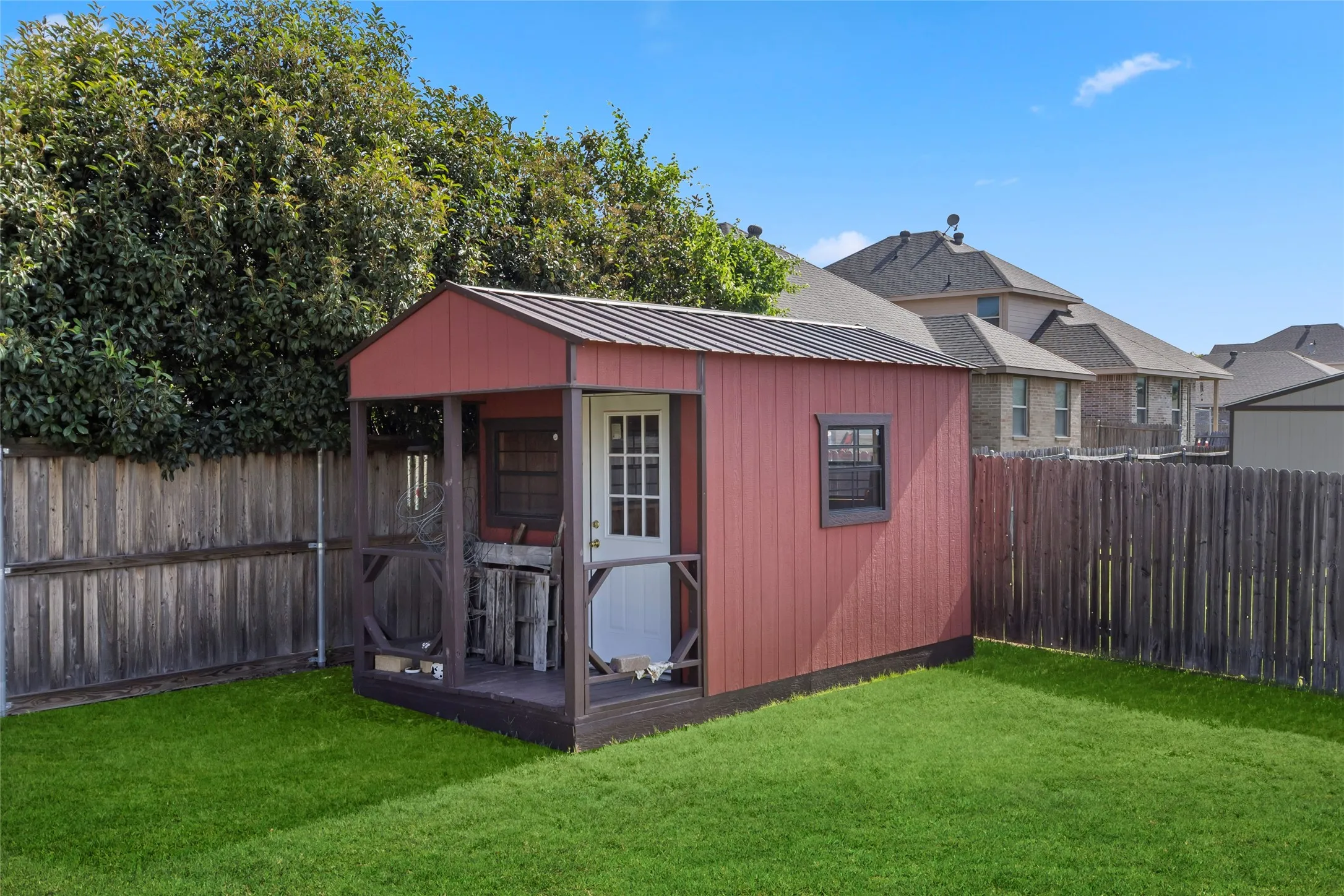 Red exterior storage shed featuring a covered porch, white entry door, and a metal roof