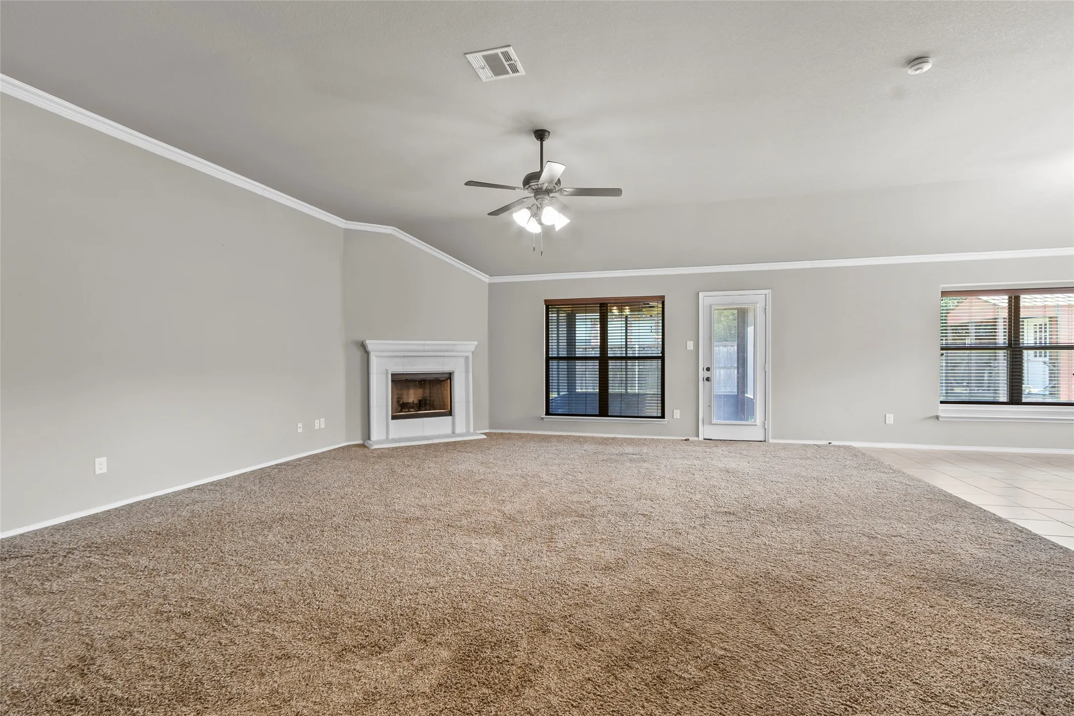 Spacious living area featuring a corner fireplace with a white mantel, ceiling fan, crown molding, and light-colored walls