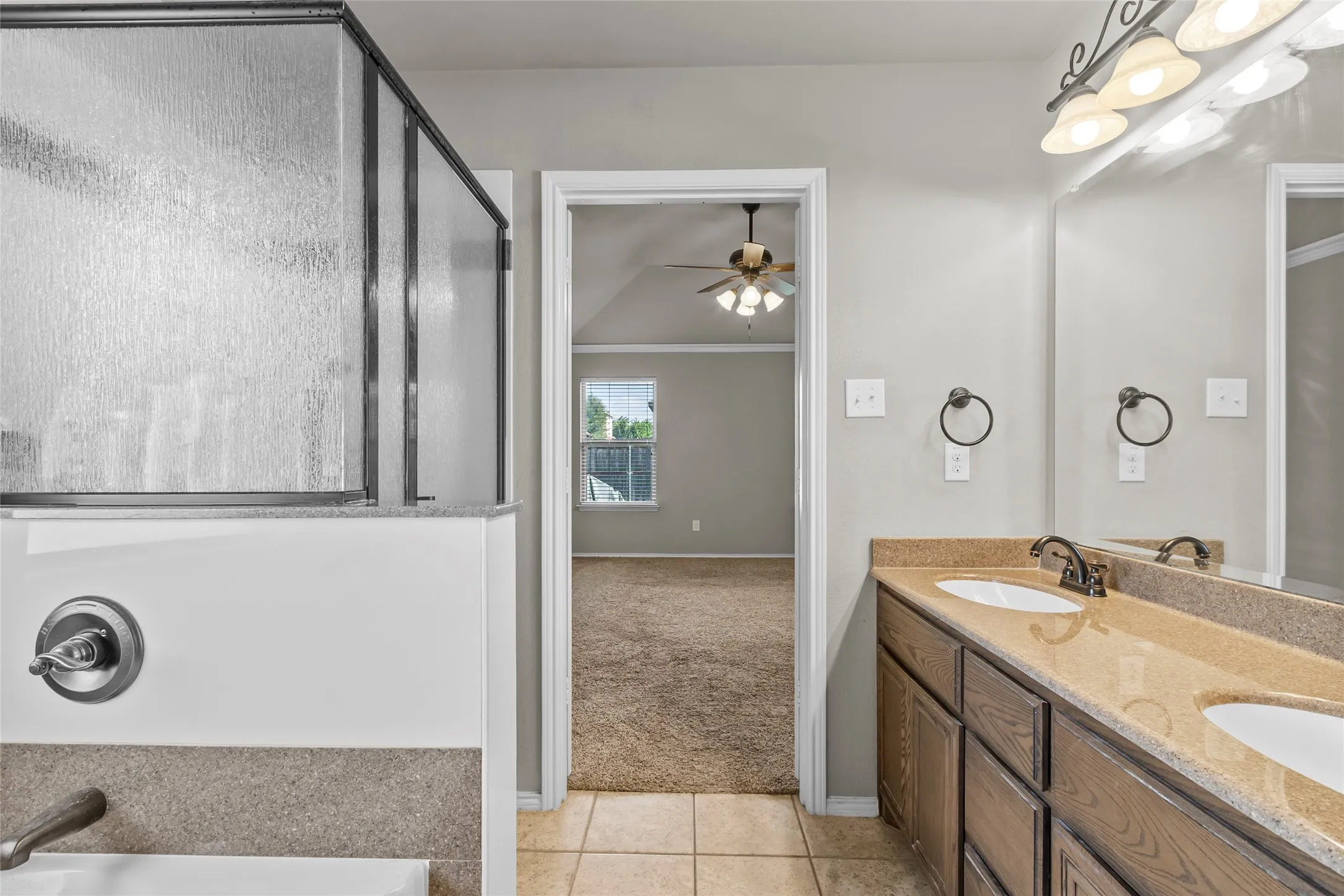 Bathroom vanity with dual sinks and bronze fixtures, complemented by a textured glass shower enclosure