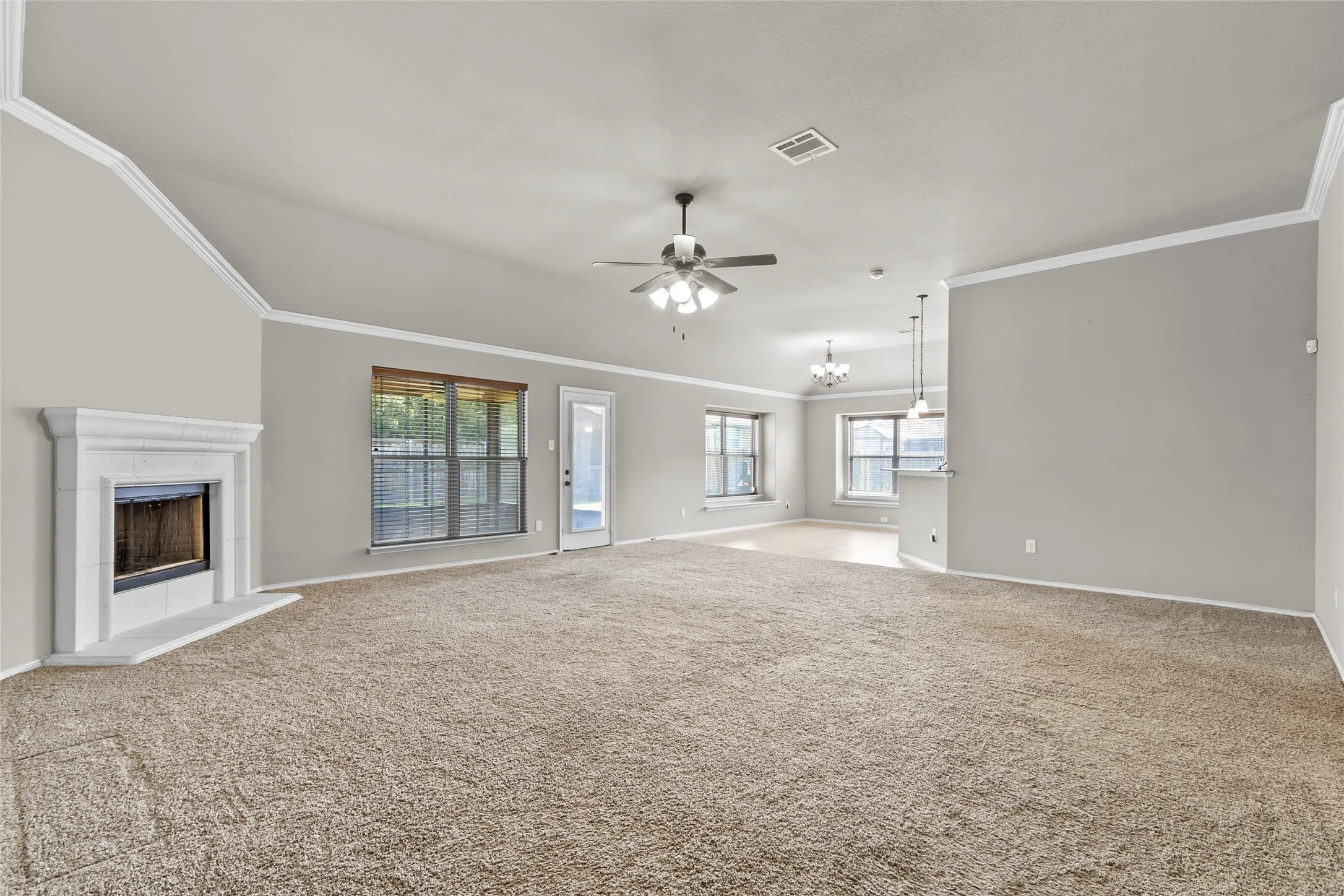 Spacious living area featuring a corner fireplace with a white mantel, vaulted ceilings with crown molding, and a ceiling fan