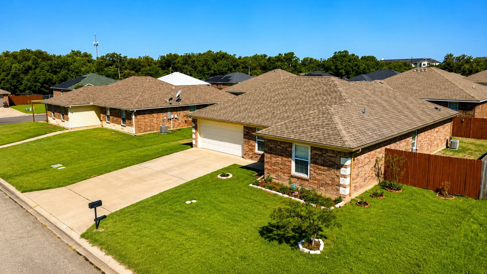 Brick exterior residence featuring an attached garage, a paved driveway, and mature landscaping