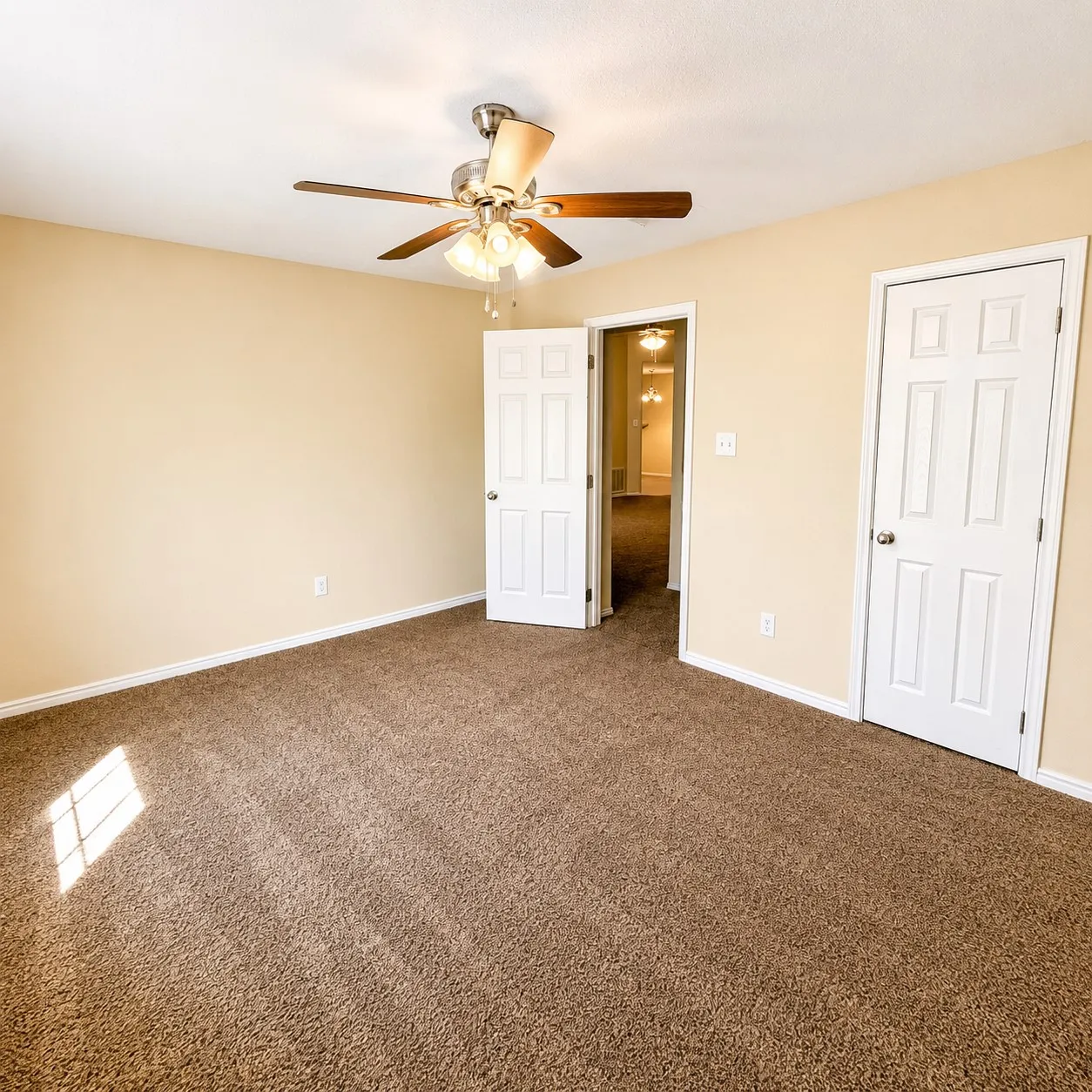 Spacious room with plush brown carpeting, light tan wall paint, and white trim