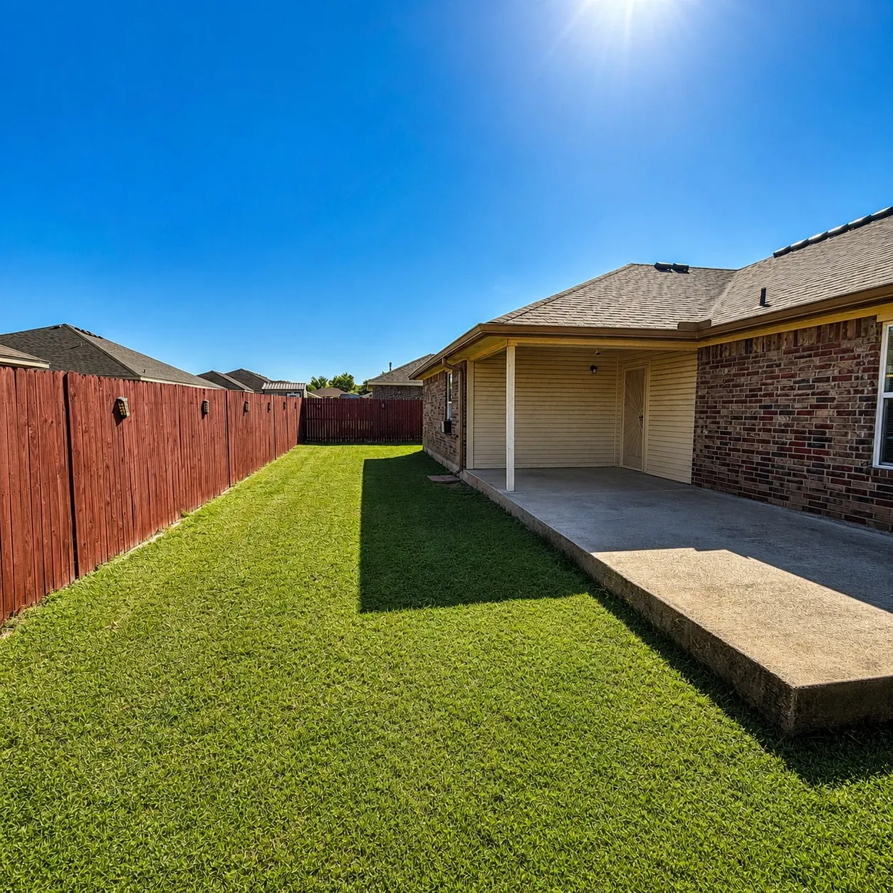 Expansive backyard featuring a covered patio with concrete flooring, a lush green lawn, and a privacy fence
