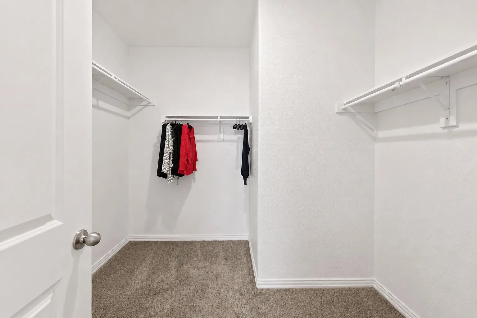 Spacious walk-in closet with carpeted flooring, multiple white wire shelving units, and ample hanging rods