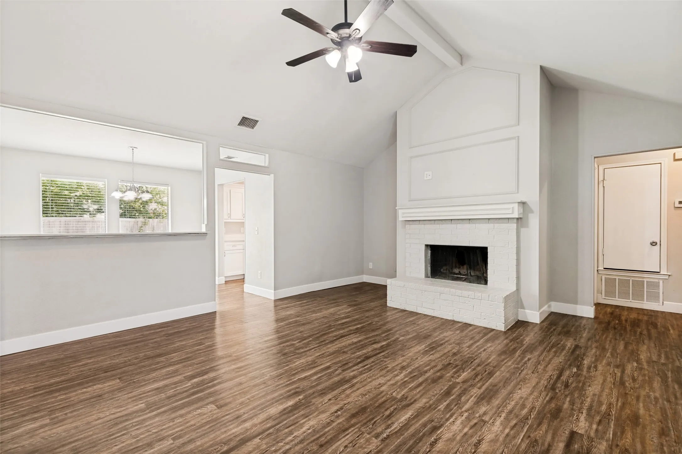 Vaulted ceiling with exposed beam, wood-finish flooring, and a brick fireplace with white painted finish
