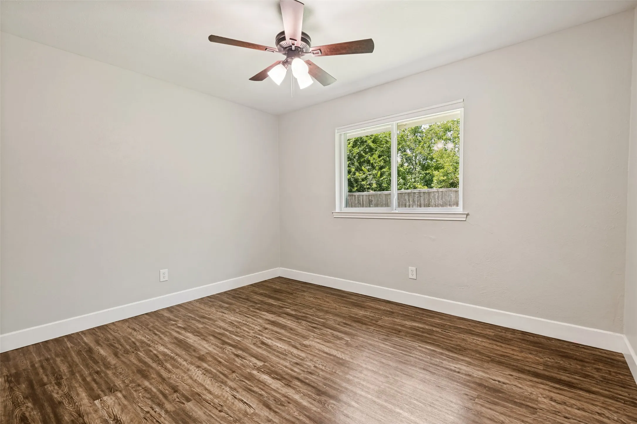 Interior room featuring wood-finish flooring, light gray walls, a window with a white frame, and a ceiling fan with light fixture