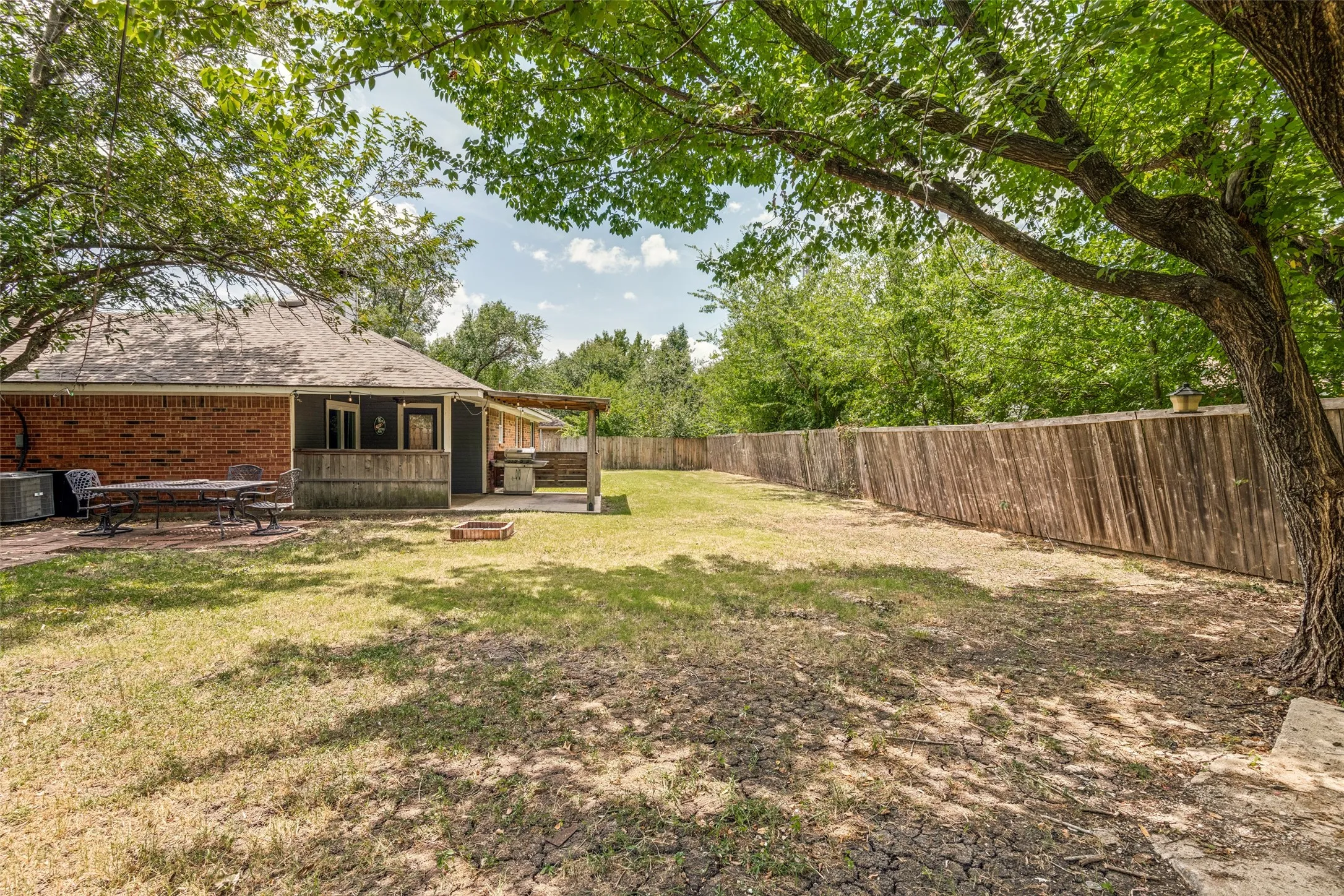 Expansive backyard space featuring mature trees, a full privacy fence, and a brick paver patio