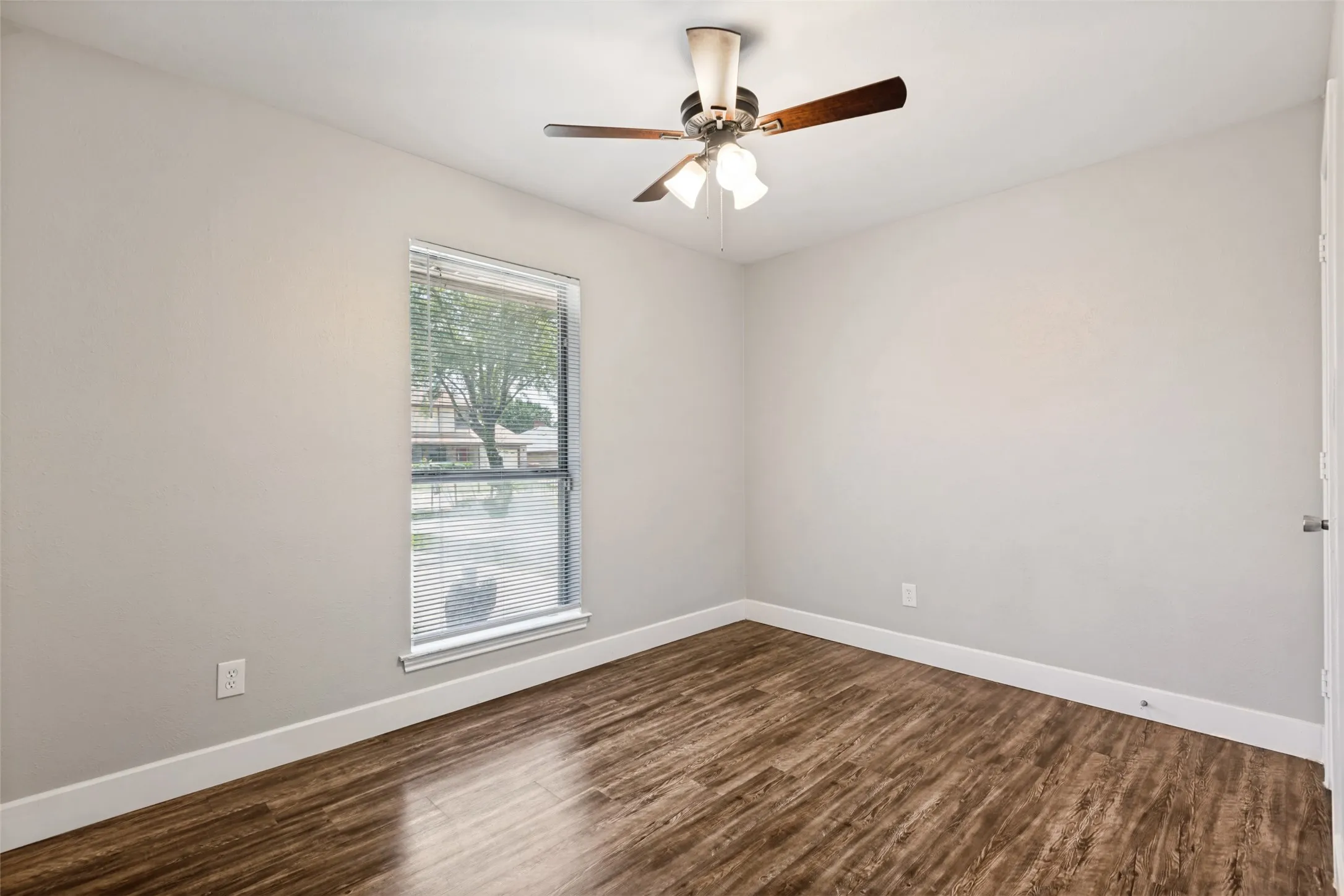 Room featuring wood-finish flooring, light gray walls, a window with blinds, and a ceiling fan with integrated lighting