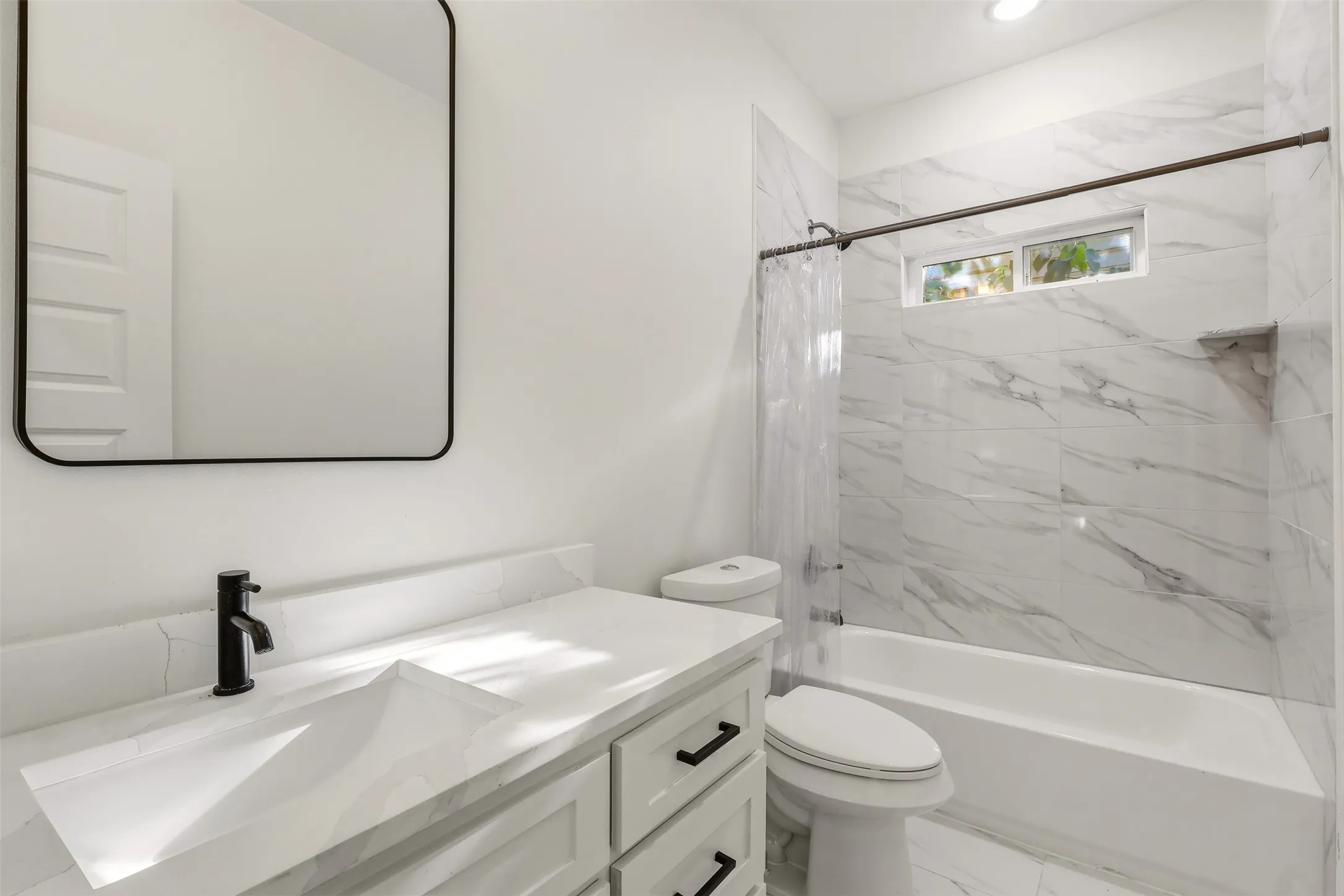 Modern bathroom featuring a white vanity with integrated sink, matte black hardware, and a framed rectangular mirror