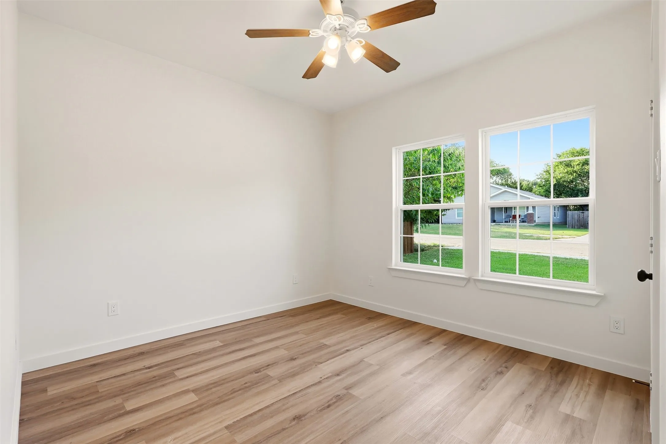 Spacious room featuring wood-finish flooring, white walls, two large windows, and a ceiling fan with light fixture