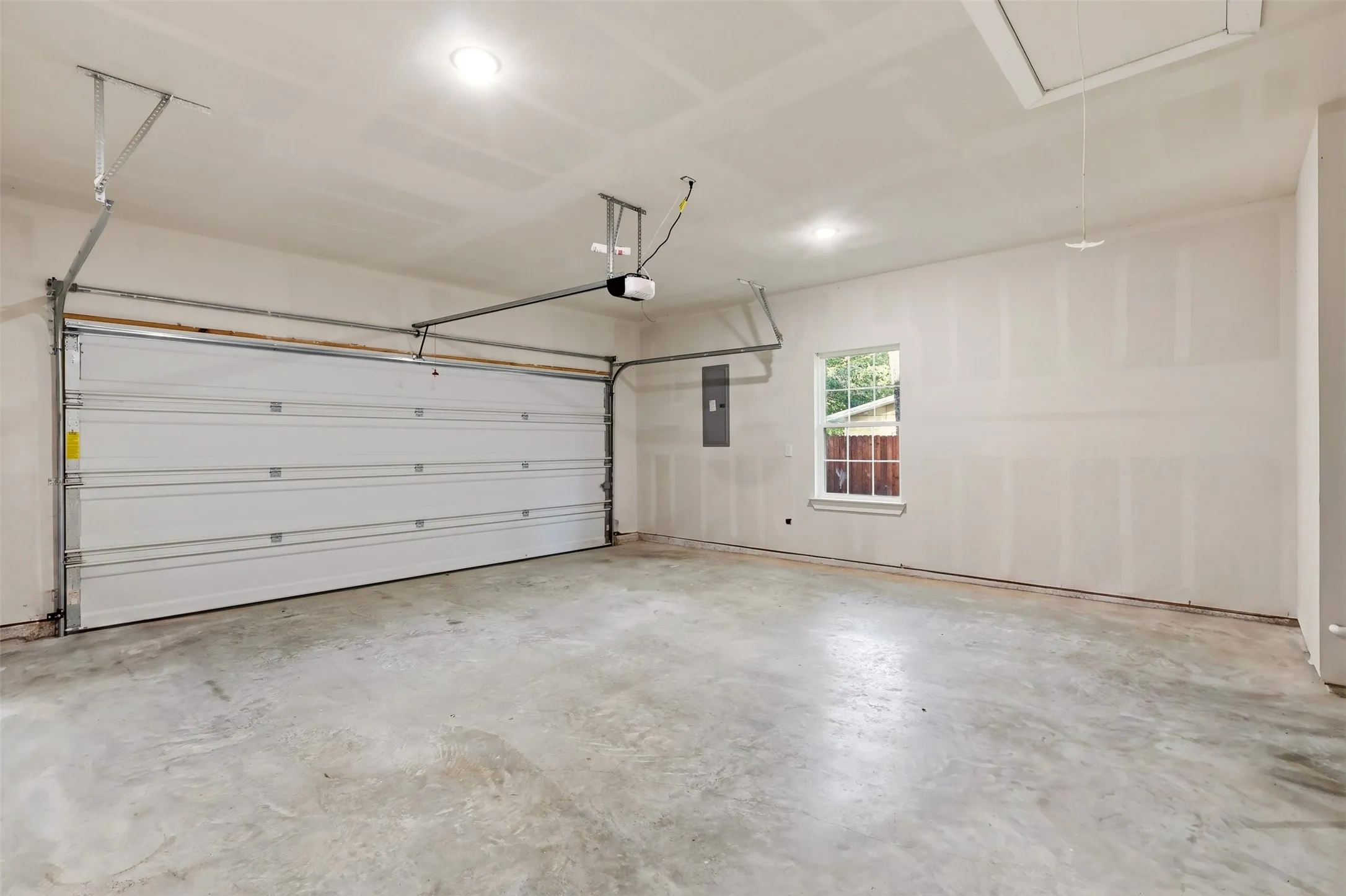 Spacious garage featuring a white sectional garage door with opener, concrete flooring, recessed lighting, a single window, and an attic access panel