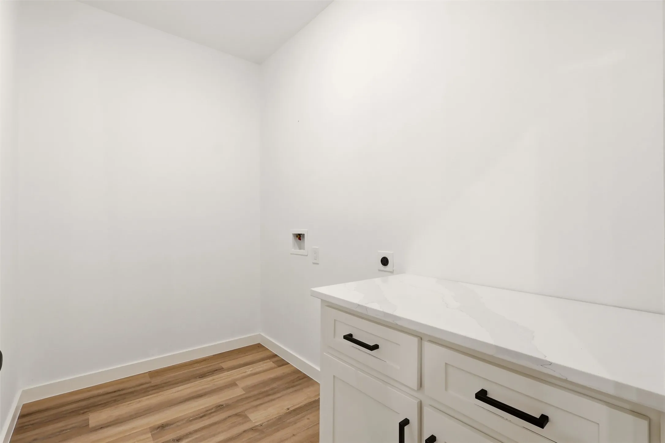 Bright white utility space featuring wood-finish flooring, white baseboards, and a built-in cabinet with a white​​‌​​​​‌​​‌‌​‌‌​​​‌‌​‌​‌​‌​​​‌​​ countertop