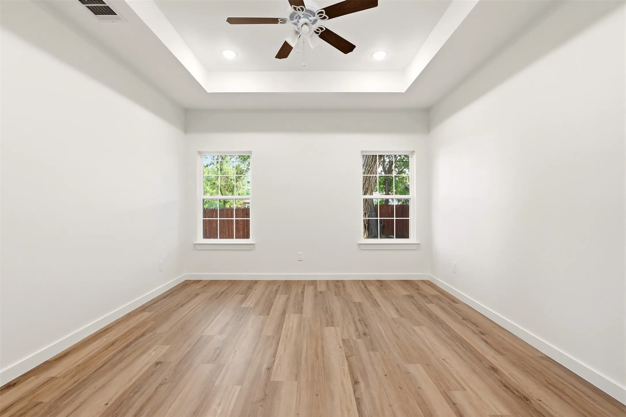 Spacious room with tray ceiling, recessed lighting, wood-finish flooring, and two windows