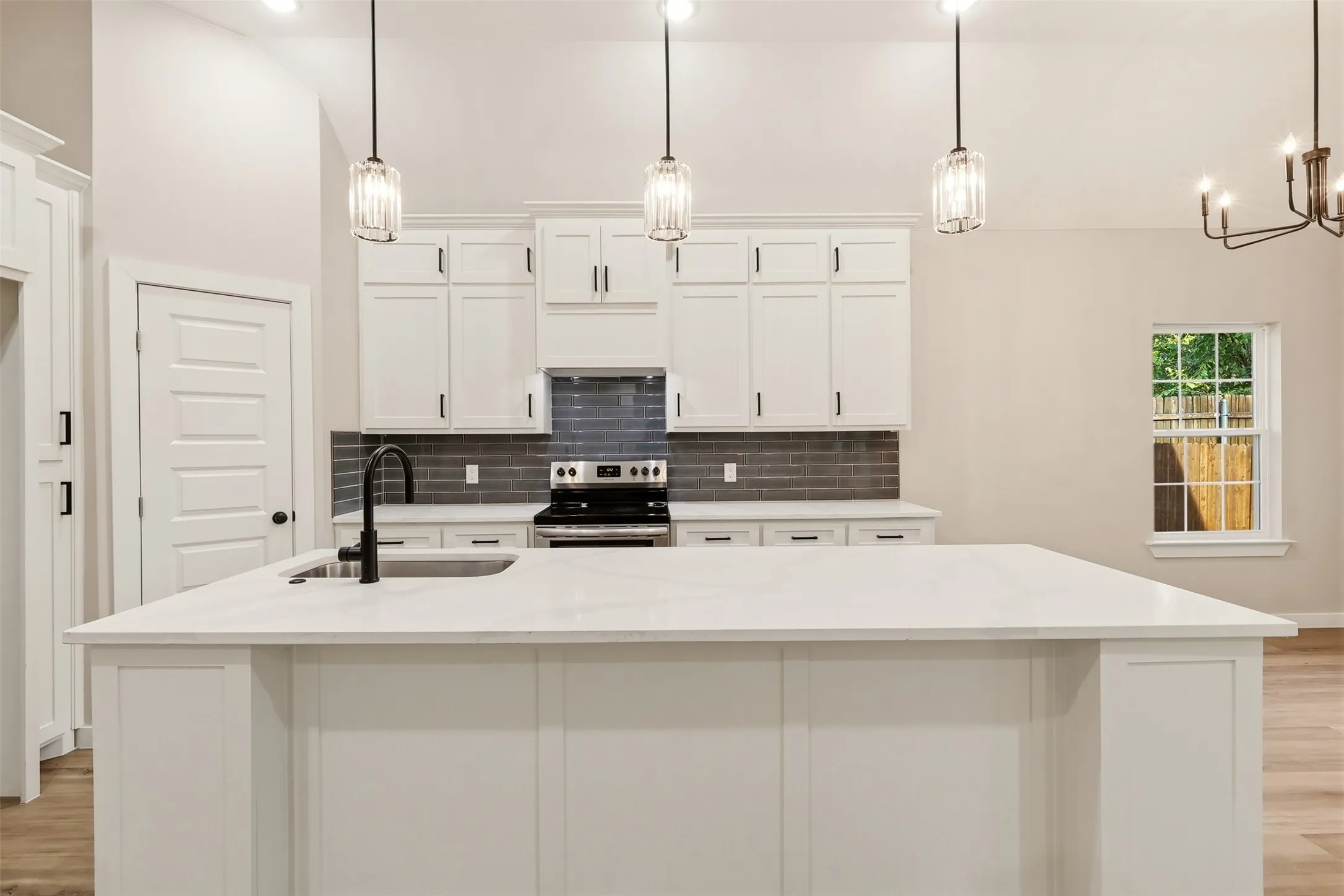 Kitchen featuring a spacious island with an undermount sink and matte black faucet, white shaker cabinetry, dark subway tile backsplash, and stainless steel range