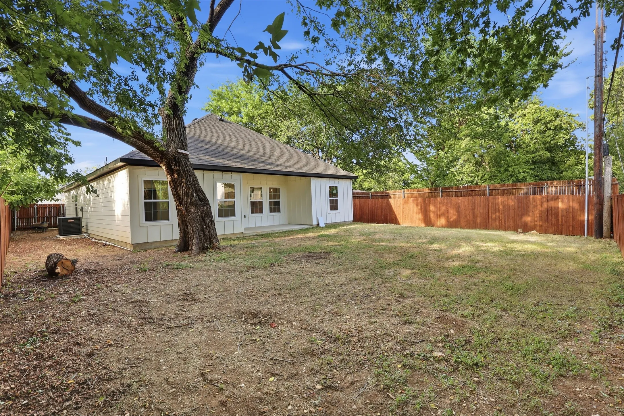 Expansive fenced yard featuring a mature tree, a concrete patio, and a white siding exterior with dark trim