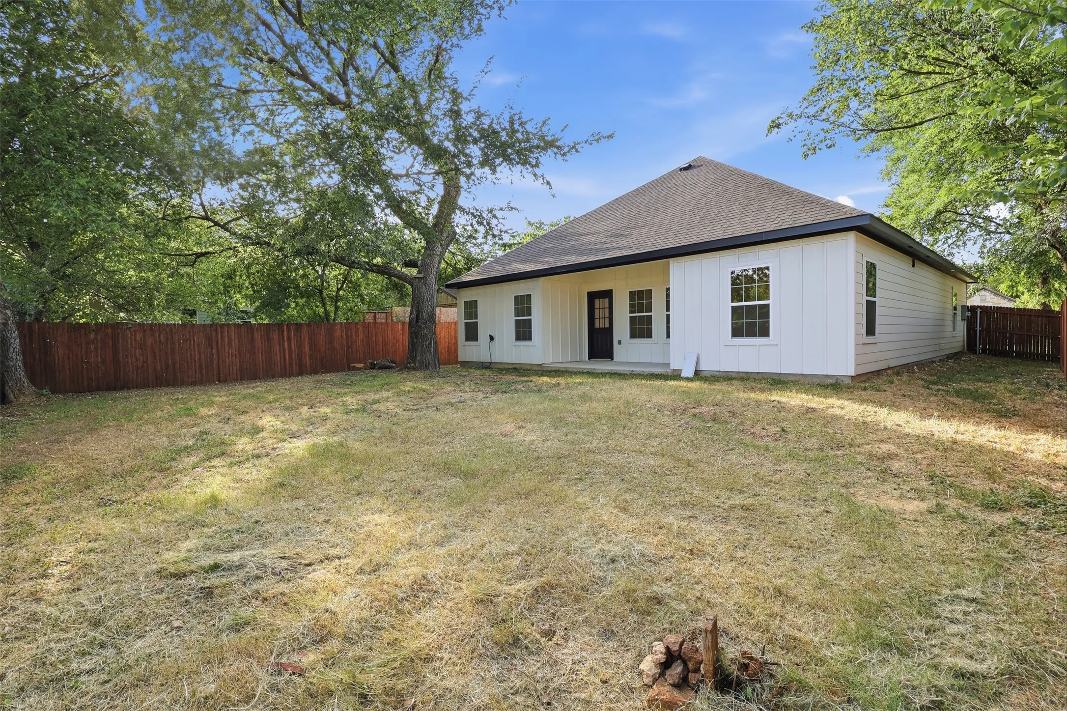 Expansive backyard featuring a privacy fence, mature trees, and a concrete patio