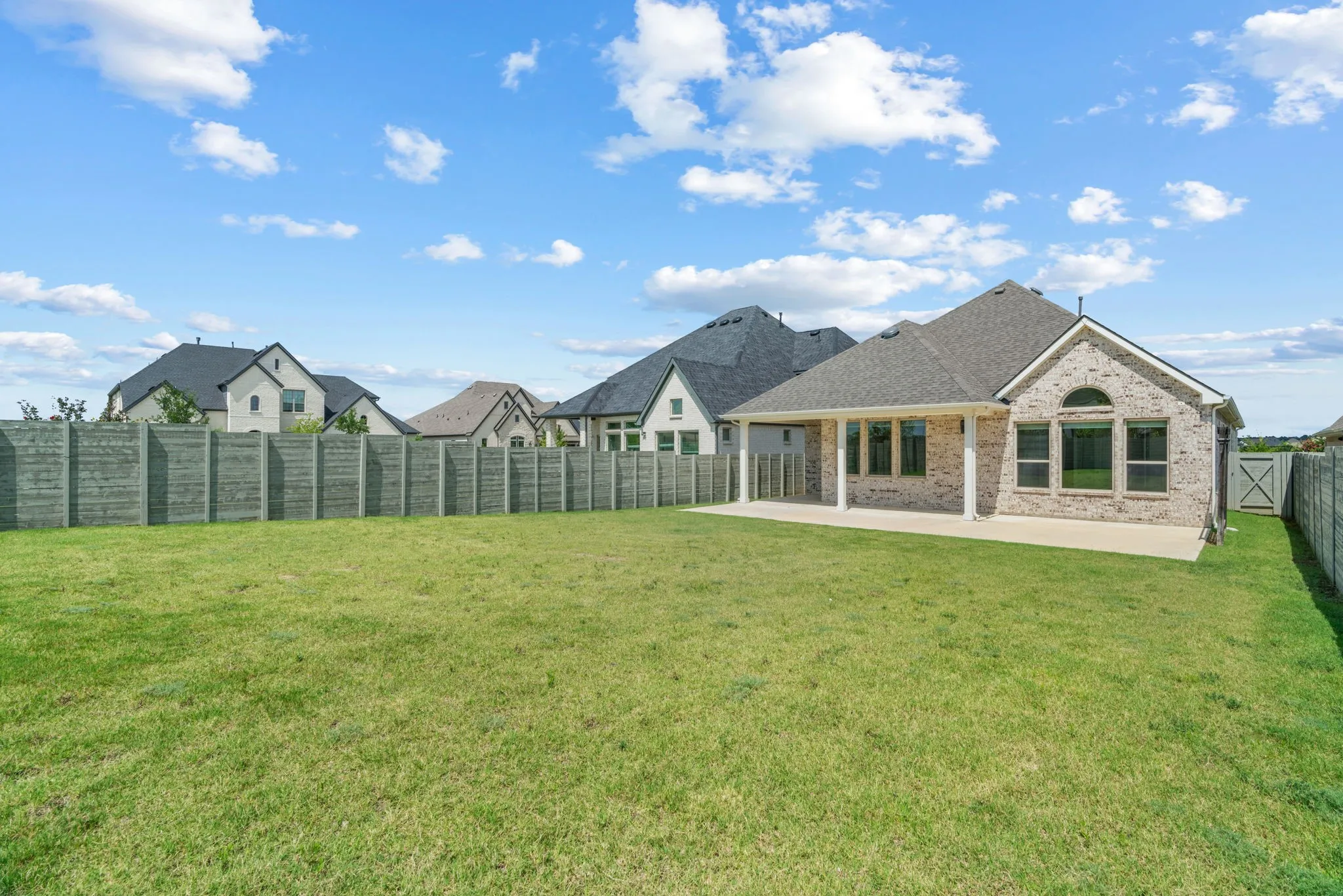 Expansive backyard featuring a large green lawn, a covered patio, and a light brick exterior with a dark shingled roof