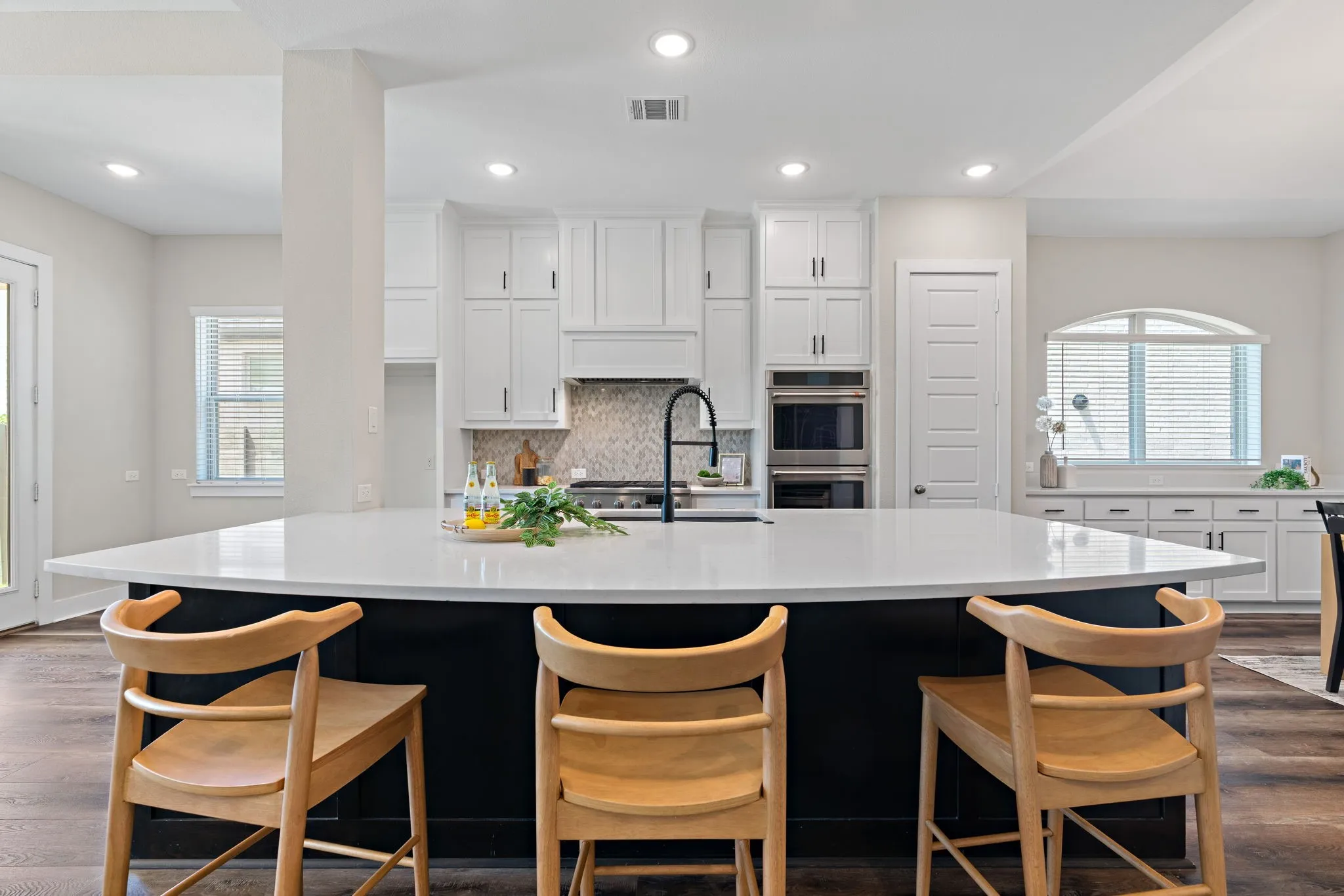 Expansive kitchen island with a light-toned countertop and black base, complemented by white cabinetry and stainless steel double ovens