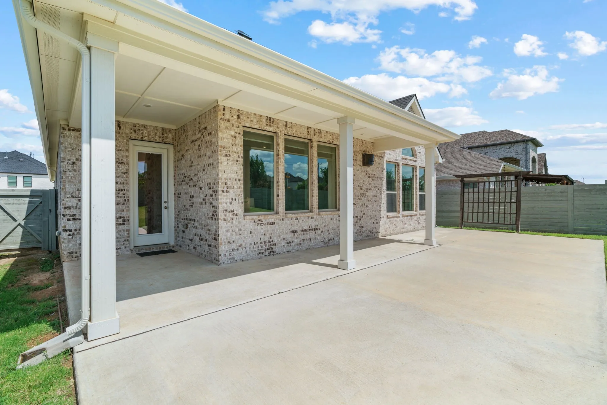 Expansive concrete patio beneath a covered porch, featuring a brick exterior, multiple windows, and a glass-paneled door