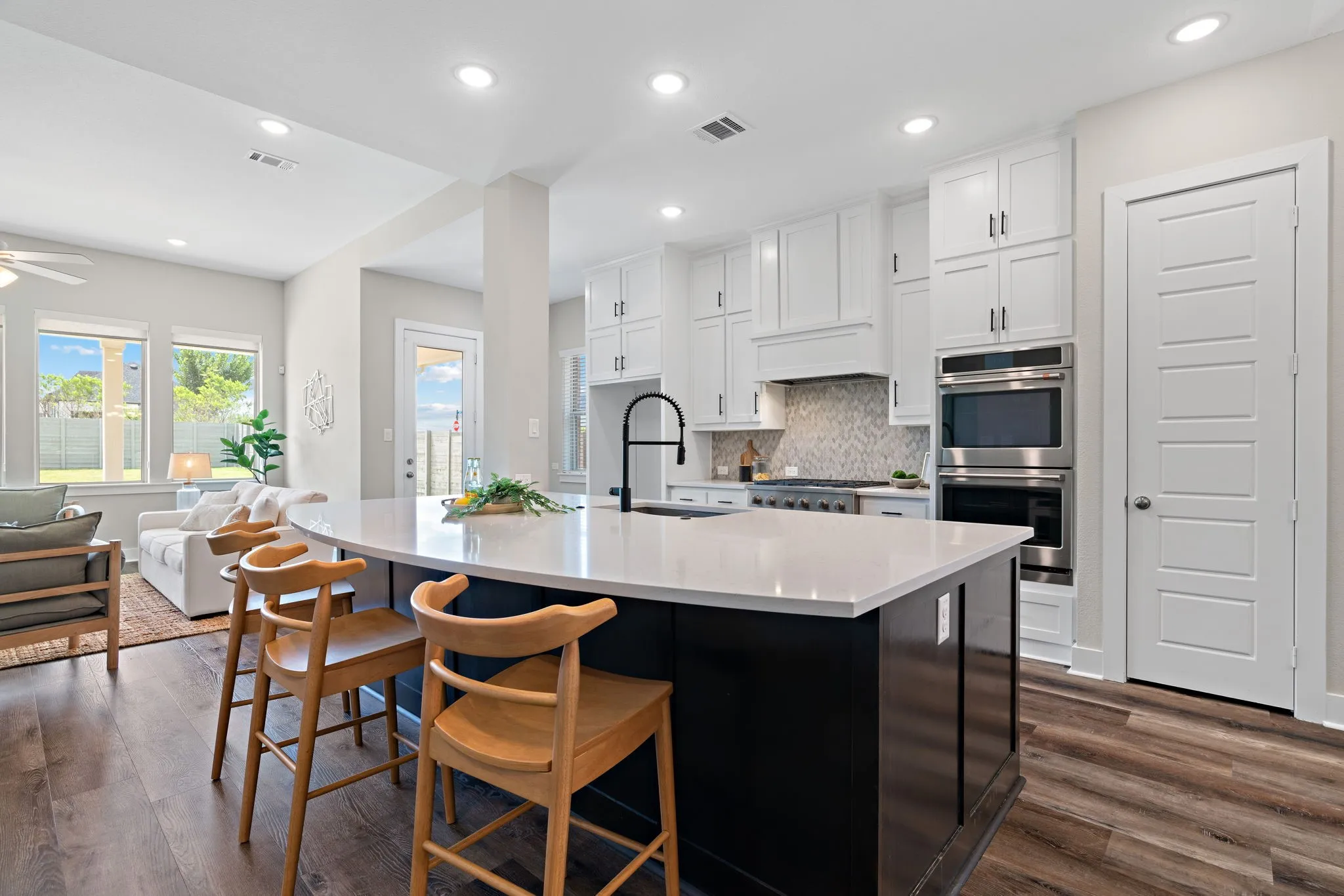 Contemporary kitchen featuring a large island with a light-colored countertop, white cabinetry, built-in stainless steel double ovens, and wood-finish flooring