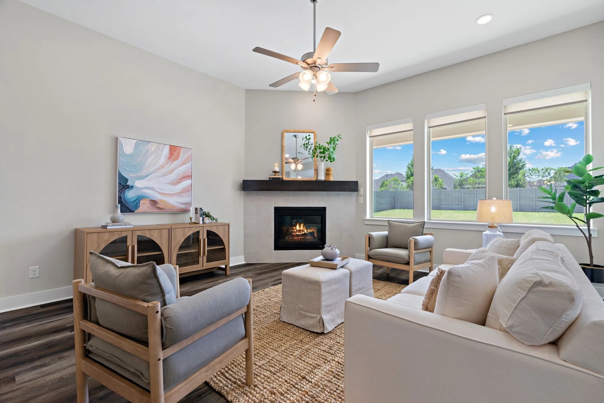 Living space featuring a corner fireplace with a dark wood mantel, wood-finish flooring, and a ceiling fan with integrated lighting
