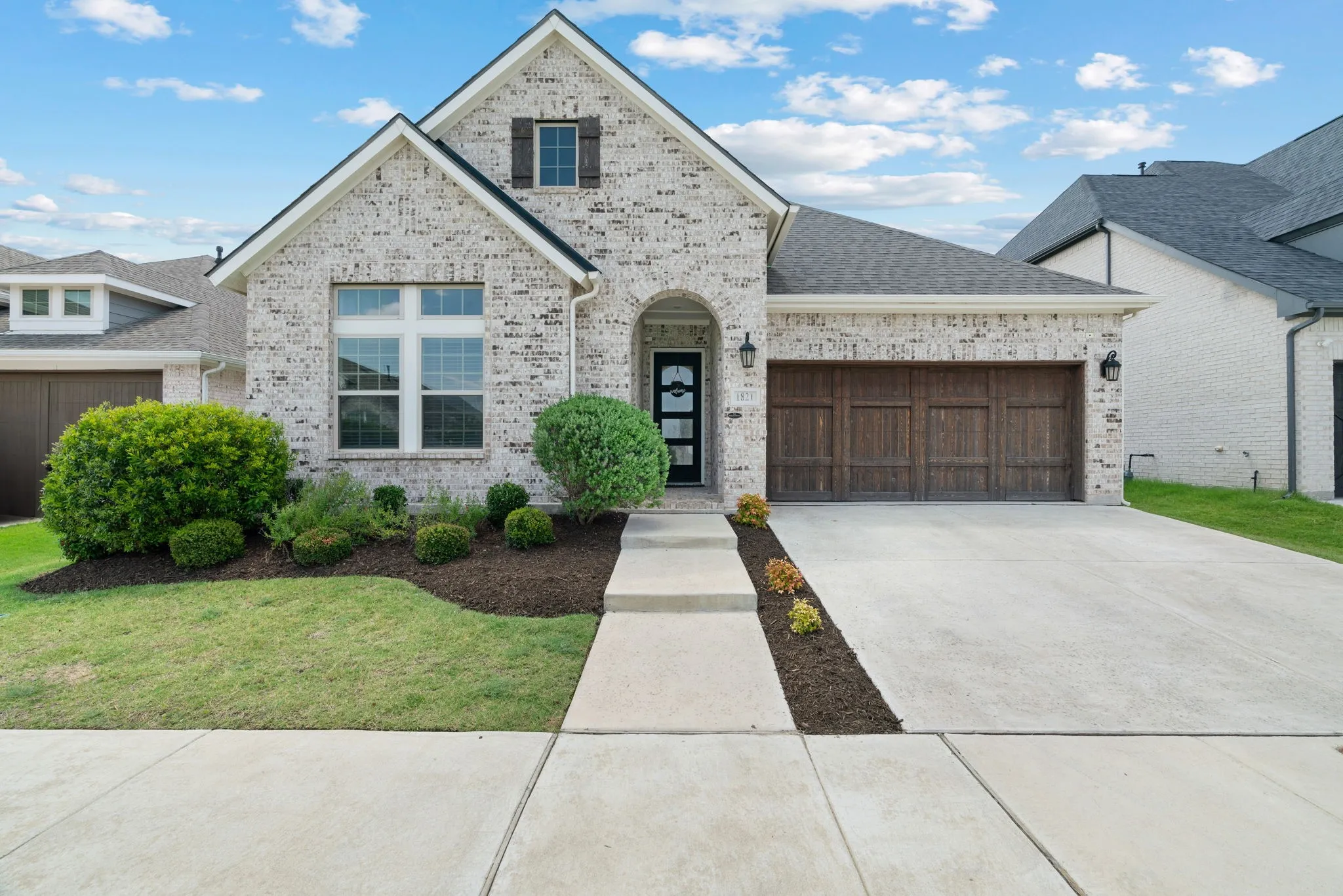 Brick facade residence with a dark wood-finish garage door, arched entryway, a composition shingle roof, and a concrete driveway