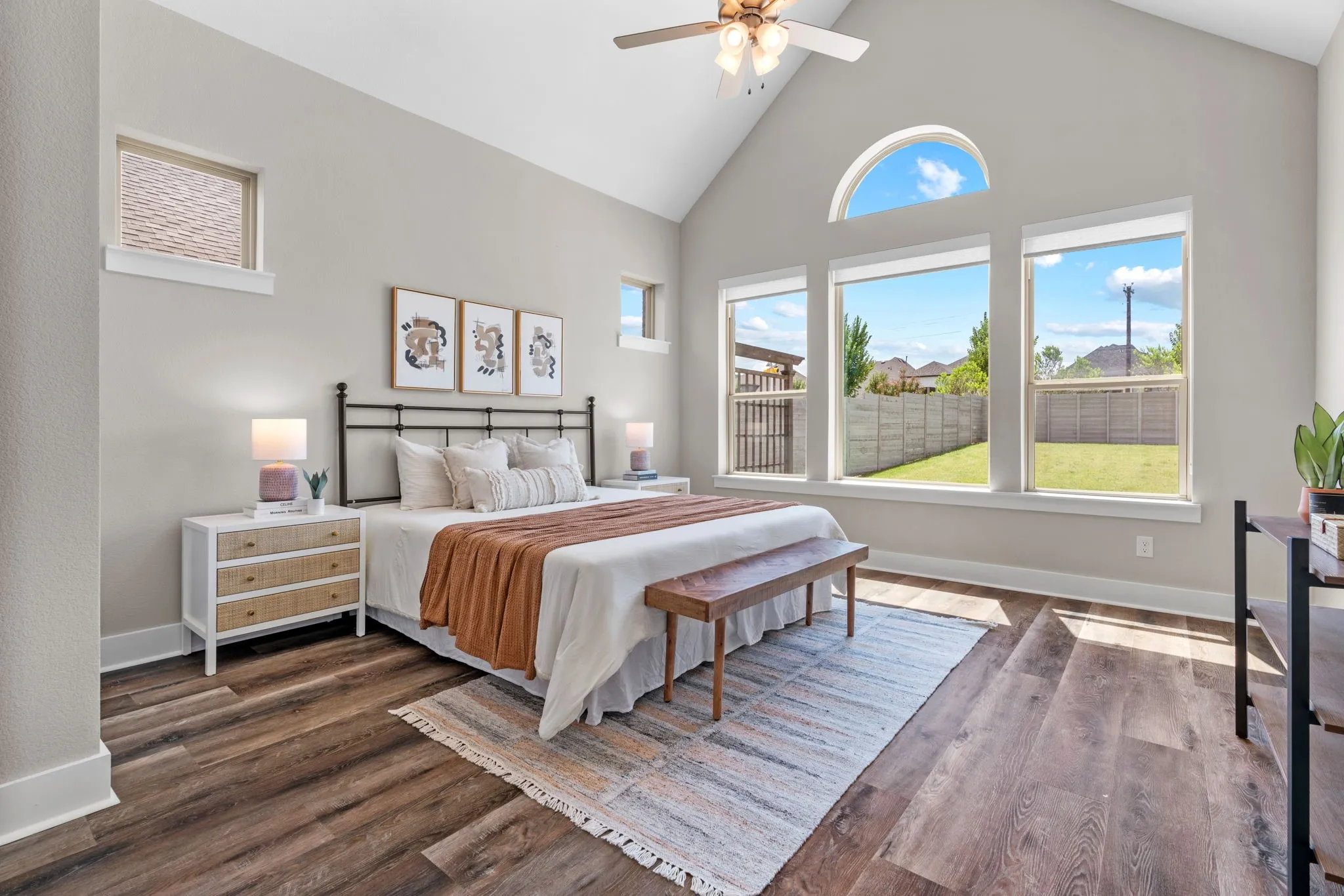 Vaulted ceiling with a ceiling fan and recessed lighting, wood-finish flooring, a wall of three picture windows, and an arched transom window