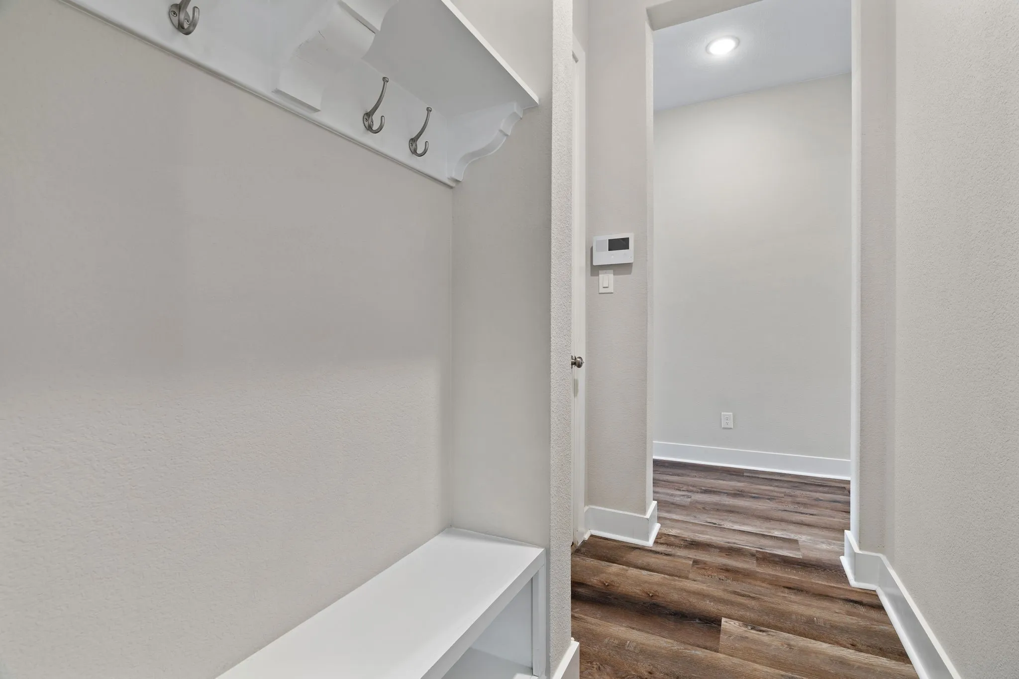 Built-in mudroom bench with shelving and coat hooks, complemented by wood-finish flooring and white baseboards