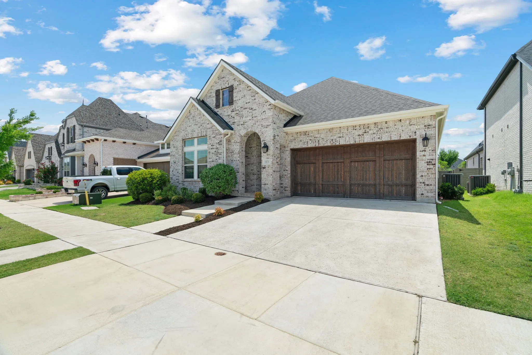 Brick exterior with a dark shingle roof, arched entryway, and a wood-look garage door