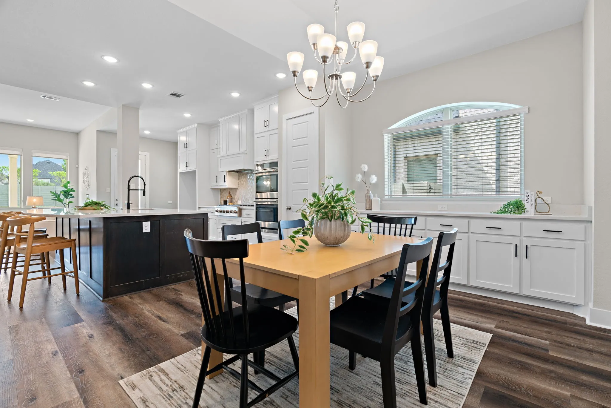 Open-concept dining area featuring wood-finish flooring, a contemporary chandelier, and a built-in buffet with white cabinetry and a light-toned countertop