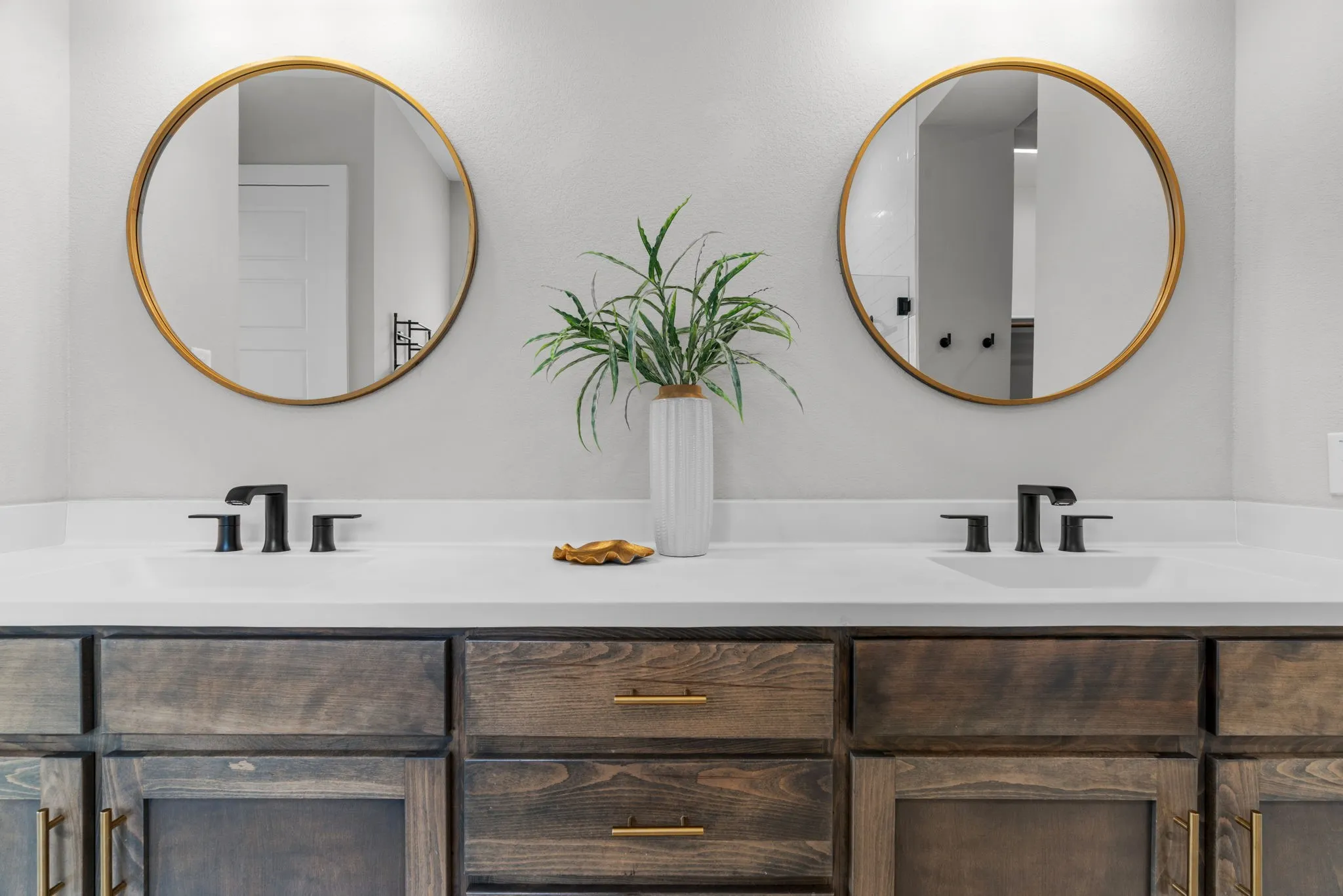 Dual vanity featuring a light-toned countertop, two round gold-framed mirrors, and dark wood-finish cabinetry with gold hardware