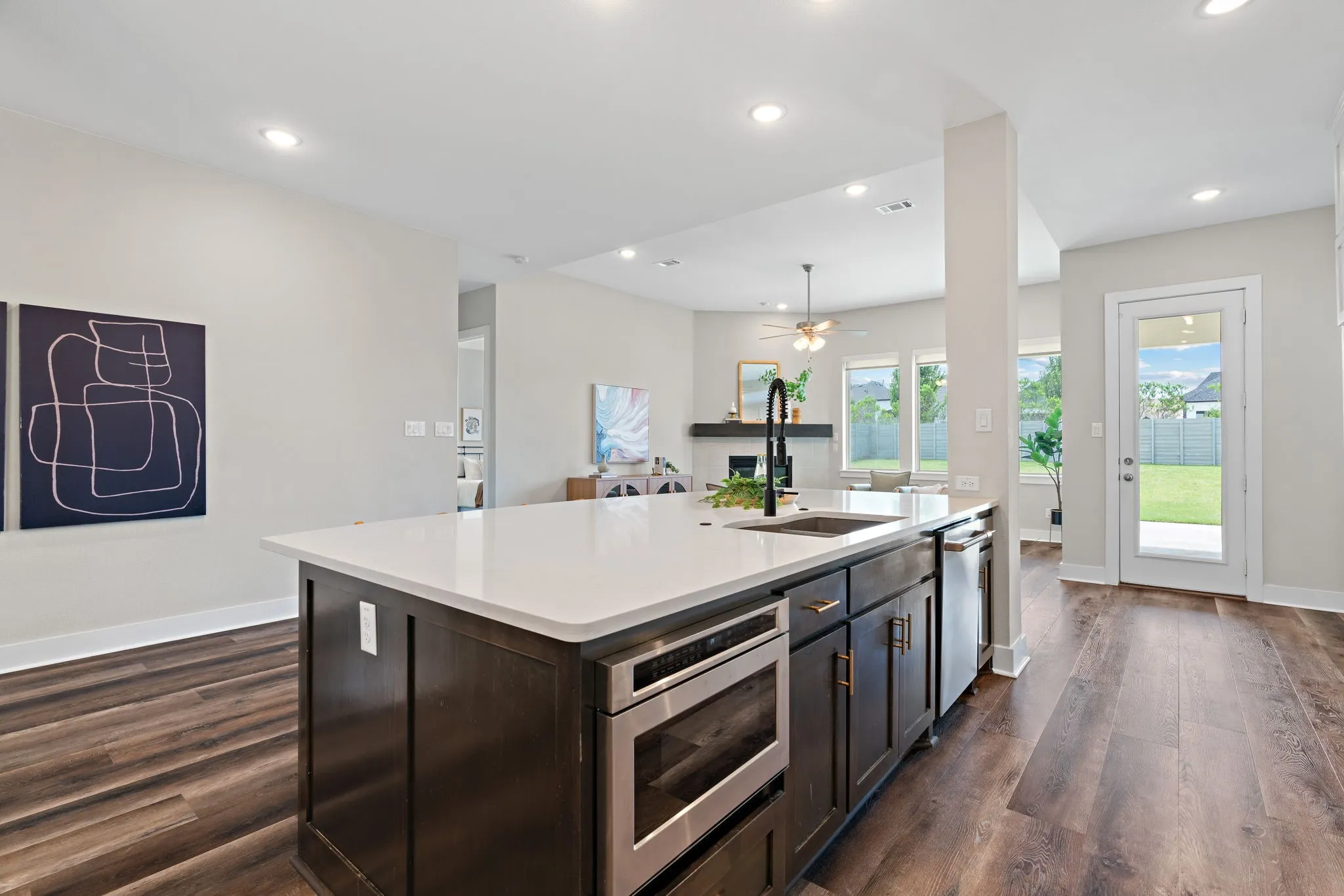 Kitchen island featuring a white countertop, undermount sink with a black gooseneck faucet, built-in microwave, and dark wood cabinetry