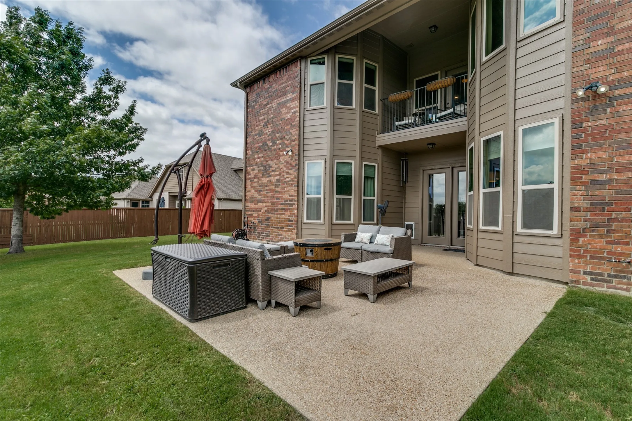 Expansive concrete patio with a spacious grass yard, featuring a privacy fence and mature tree