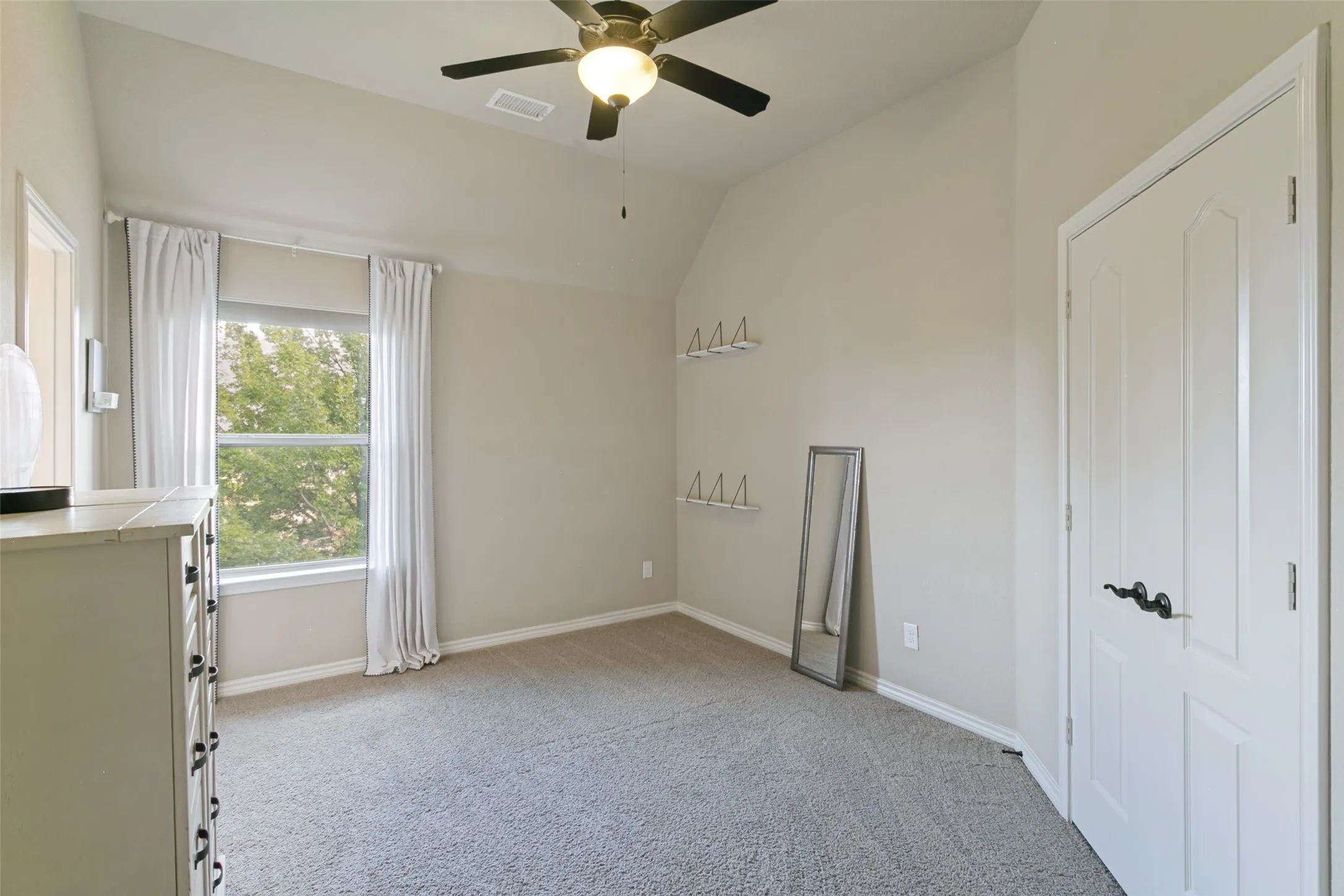 Bright third bedroom featuring neutral carpeting, ceiling fan with integrated lighting, closet with white panel doors, and large window with natural light