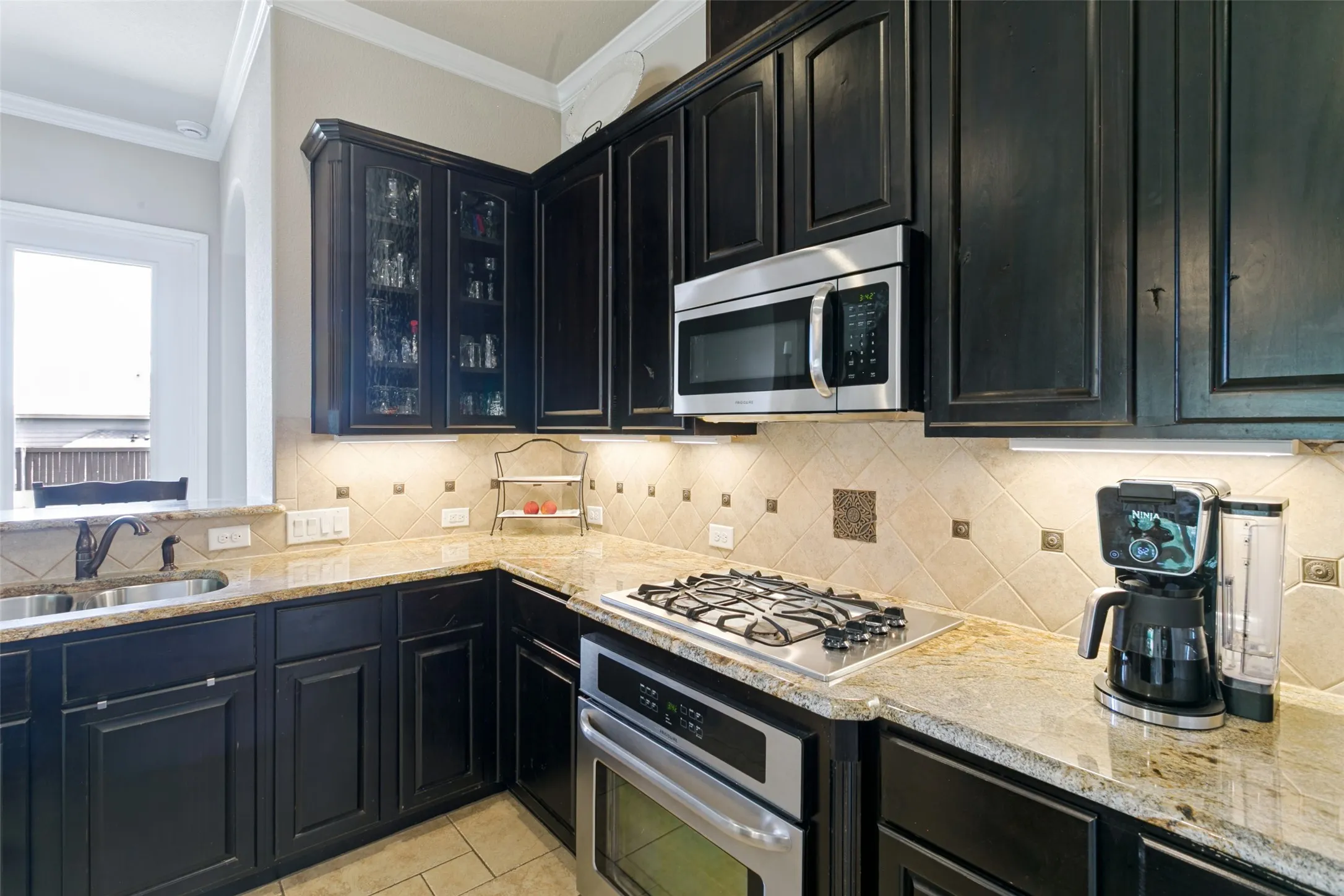 Gourmet kitchen featuring dark cabinetry with glass-front uppers, granite countertops, and a tile backsplash