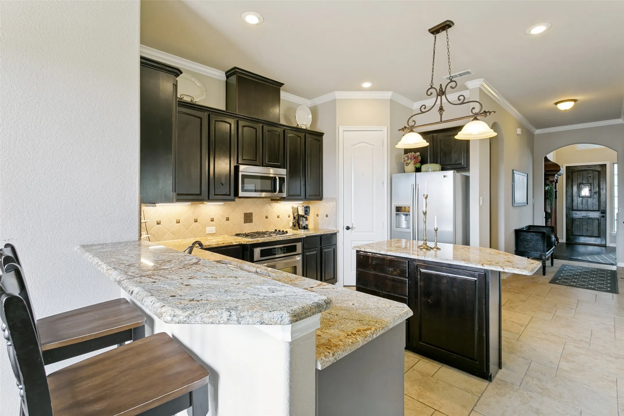 Breakfast Bar featuring dark cabinetry, stainless steel appliances, granite countertop, pendant lighting over the island, and ceramic tile flooring