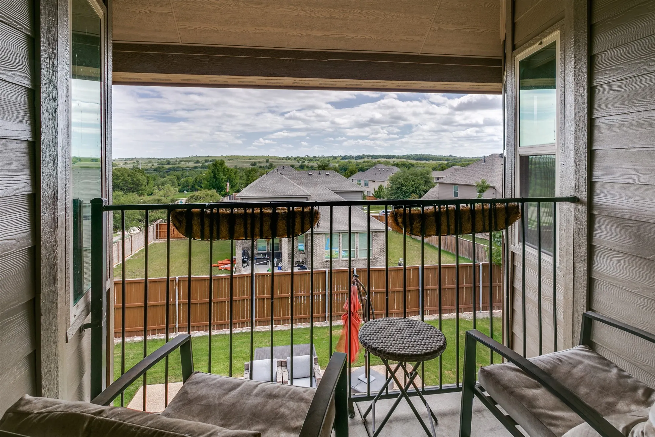 Elevated balcony with metal railing overlooking expansive grounds, mature landscaping, and open countryside