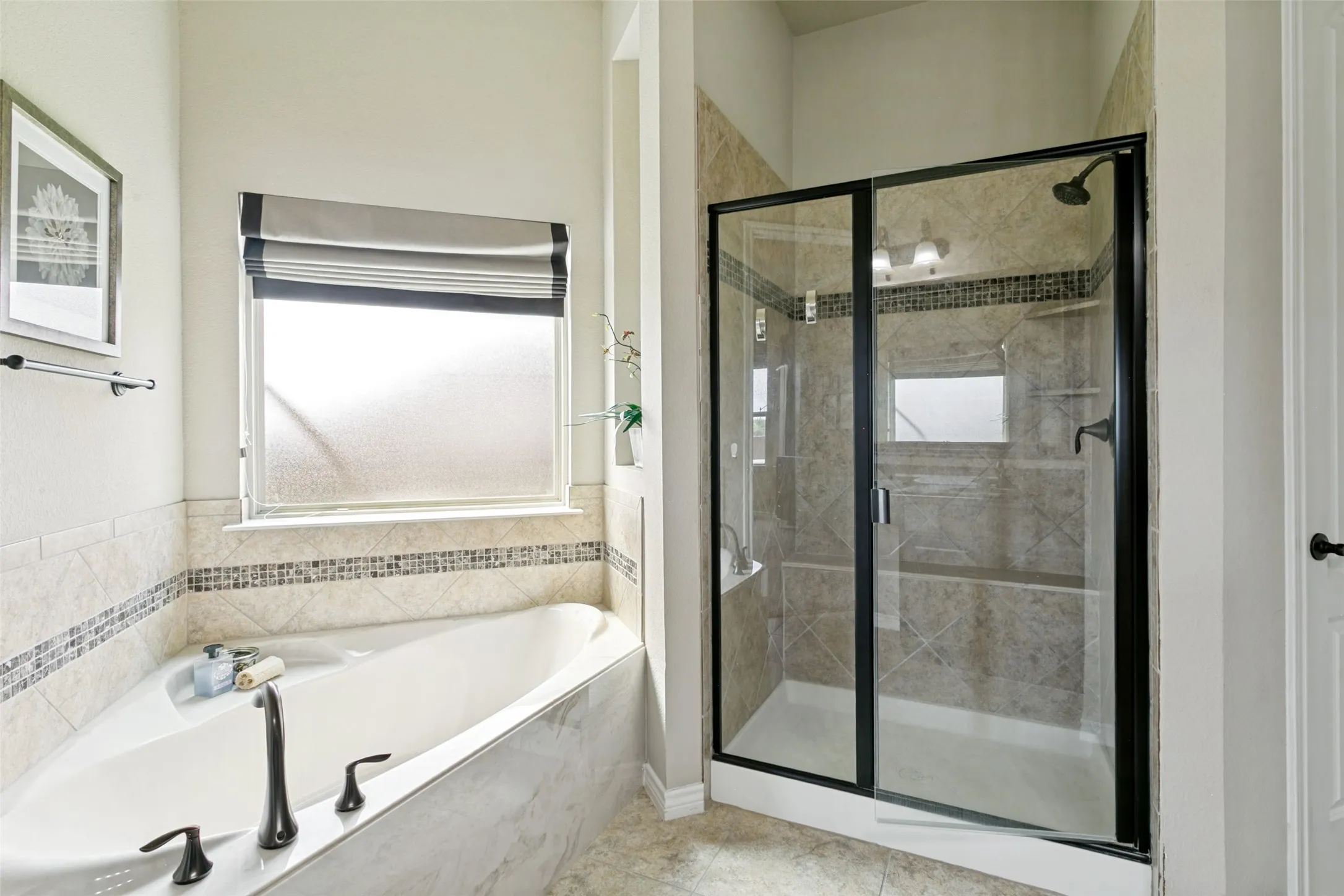 Spa-inspired primary bathroom featuring a soaking tub with oil-rubbed bronze fixtures, marble-finish surround, and a frameless glass-enclosed shower with showerhead and tile detailing