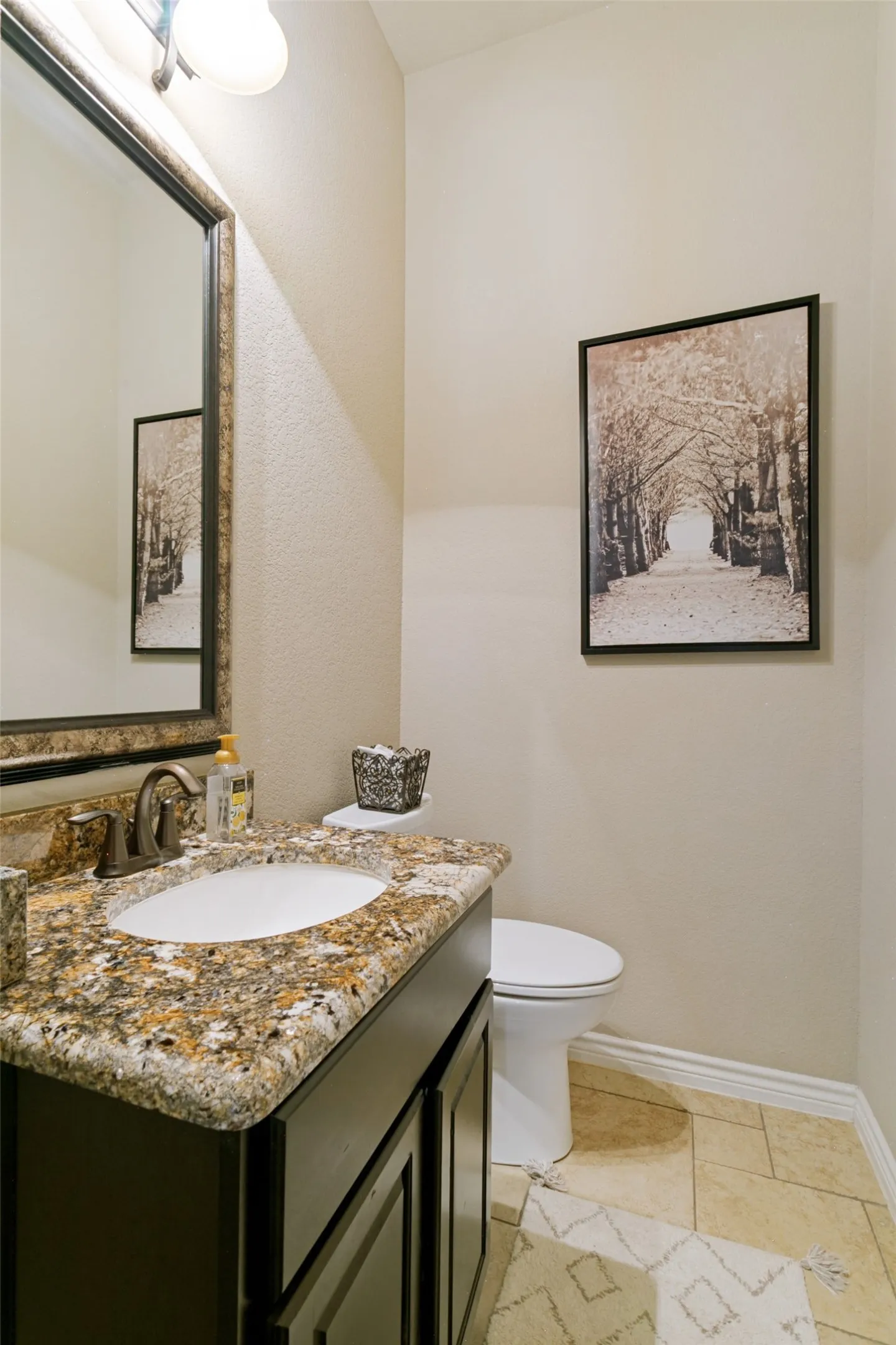 Elegant half bath showcasing a granite-topped vanity with an integrated sink, brass-finished faucet, and black cabinetry