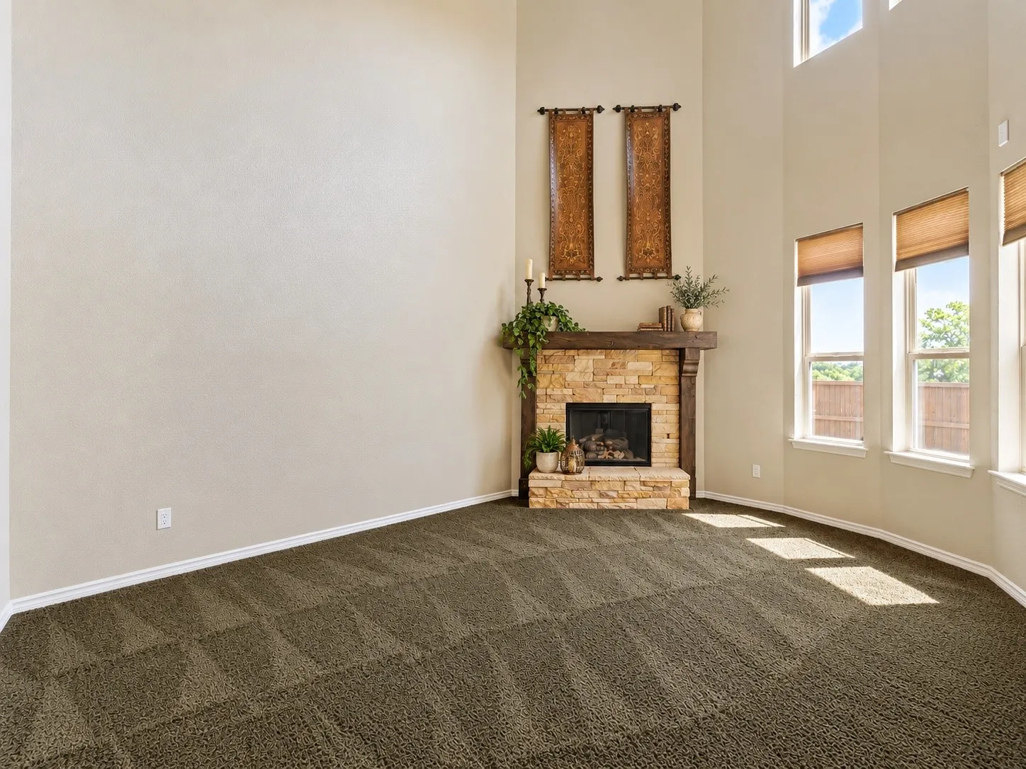 Two-story ceiling, stone fireplace with wood mantel, multiple windows with blinds, and carpet flooring