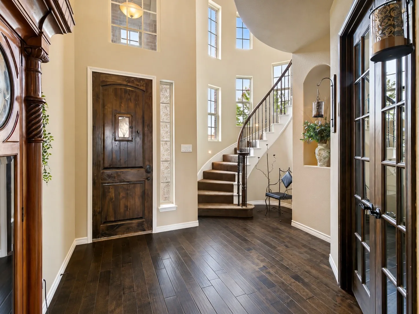 Hardwood flooring throughout, a grand wooden entry door with a decorative glass insert, a curved staircase with wrought iron balusters, and multiple arched windows