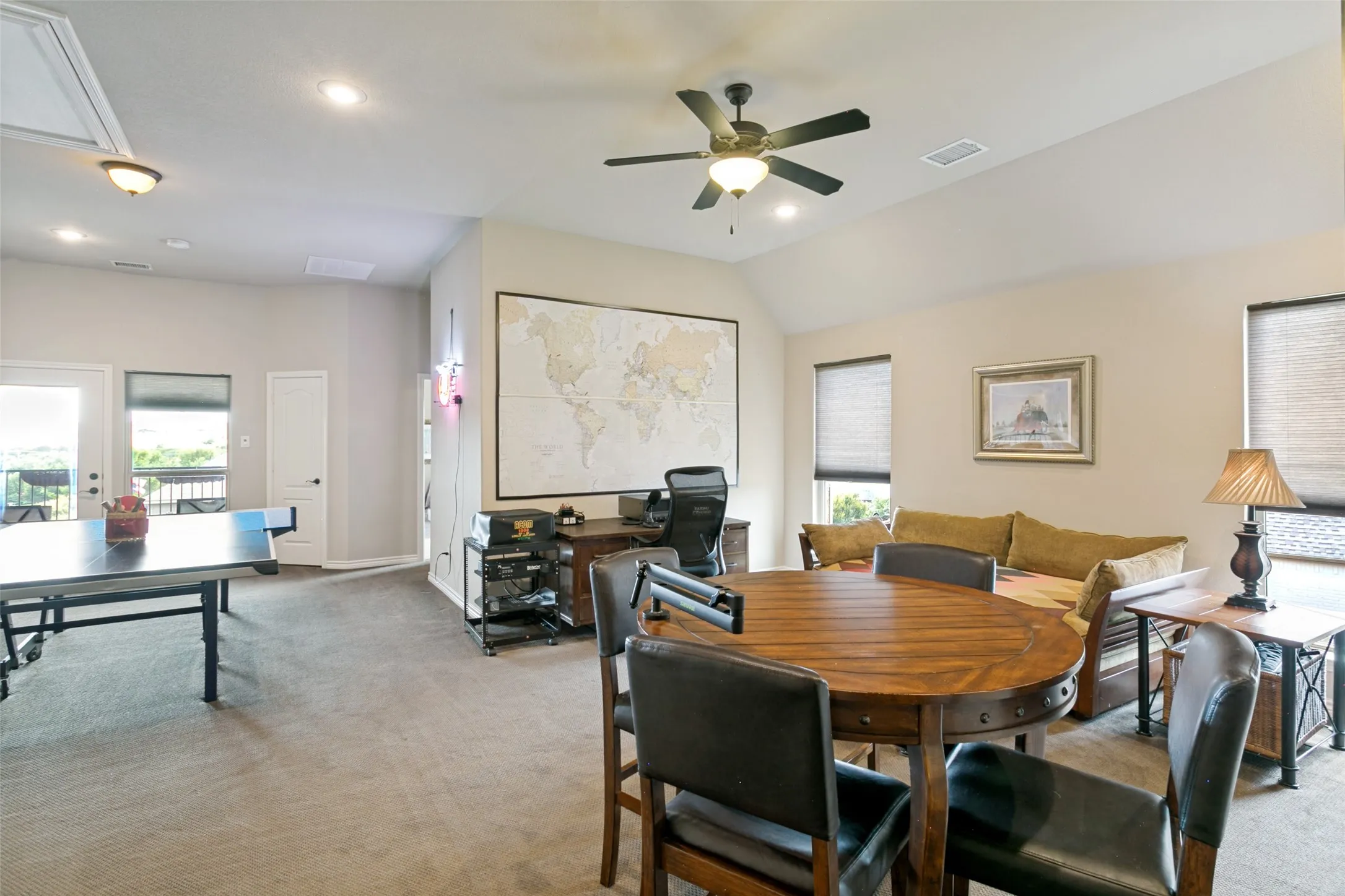 Spacious open-concept game/living area featuring  neutral carpet flooring, and abundant natural light from multiple windows