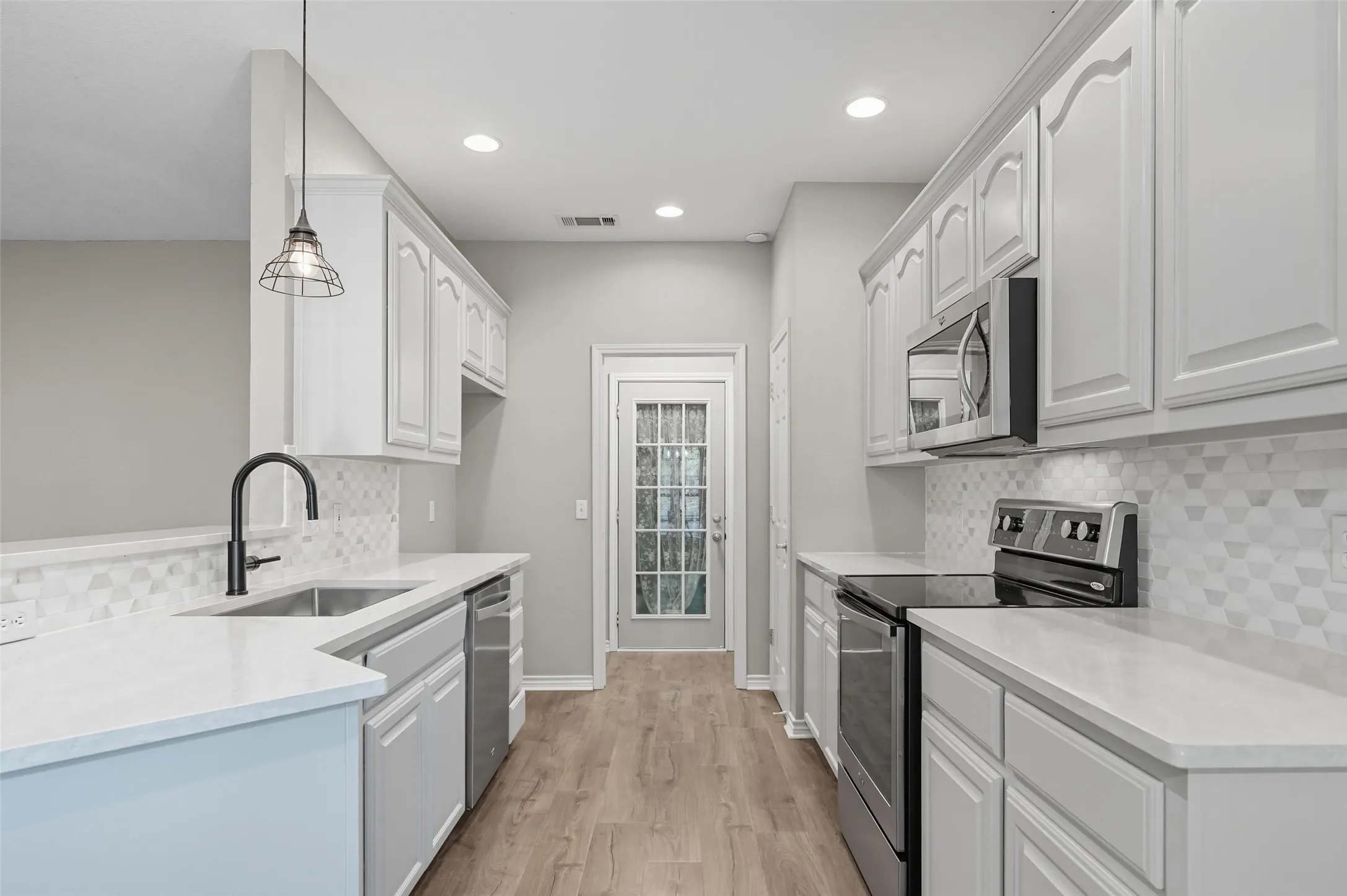 Kitchen with decorative backsplash, appliances with stainless steel finishes, light wood-style flooring, decorative light fixtures, and white cabinetry