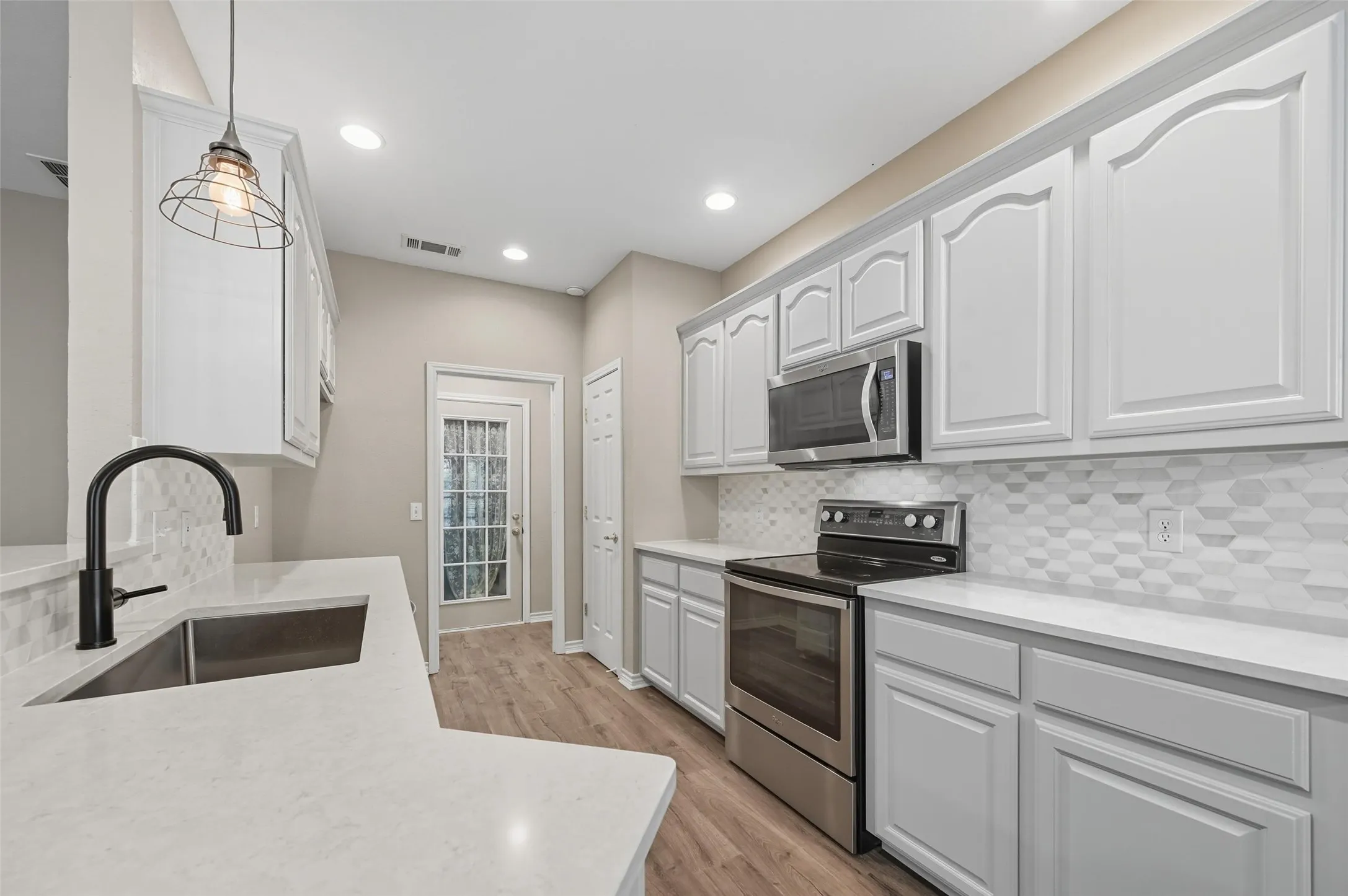 Kitchen with stainless steel appliances, tasteful backsplash, light wood-style floors, hanging light fixtures, and recessed lighting
