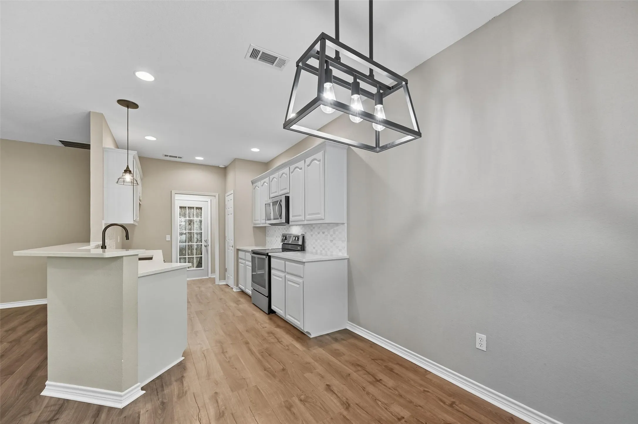 Kitchen featuring light countertops, stainless steel appliances, hanging light fixtures, white cabinets, and recessed lighting
