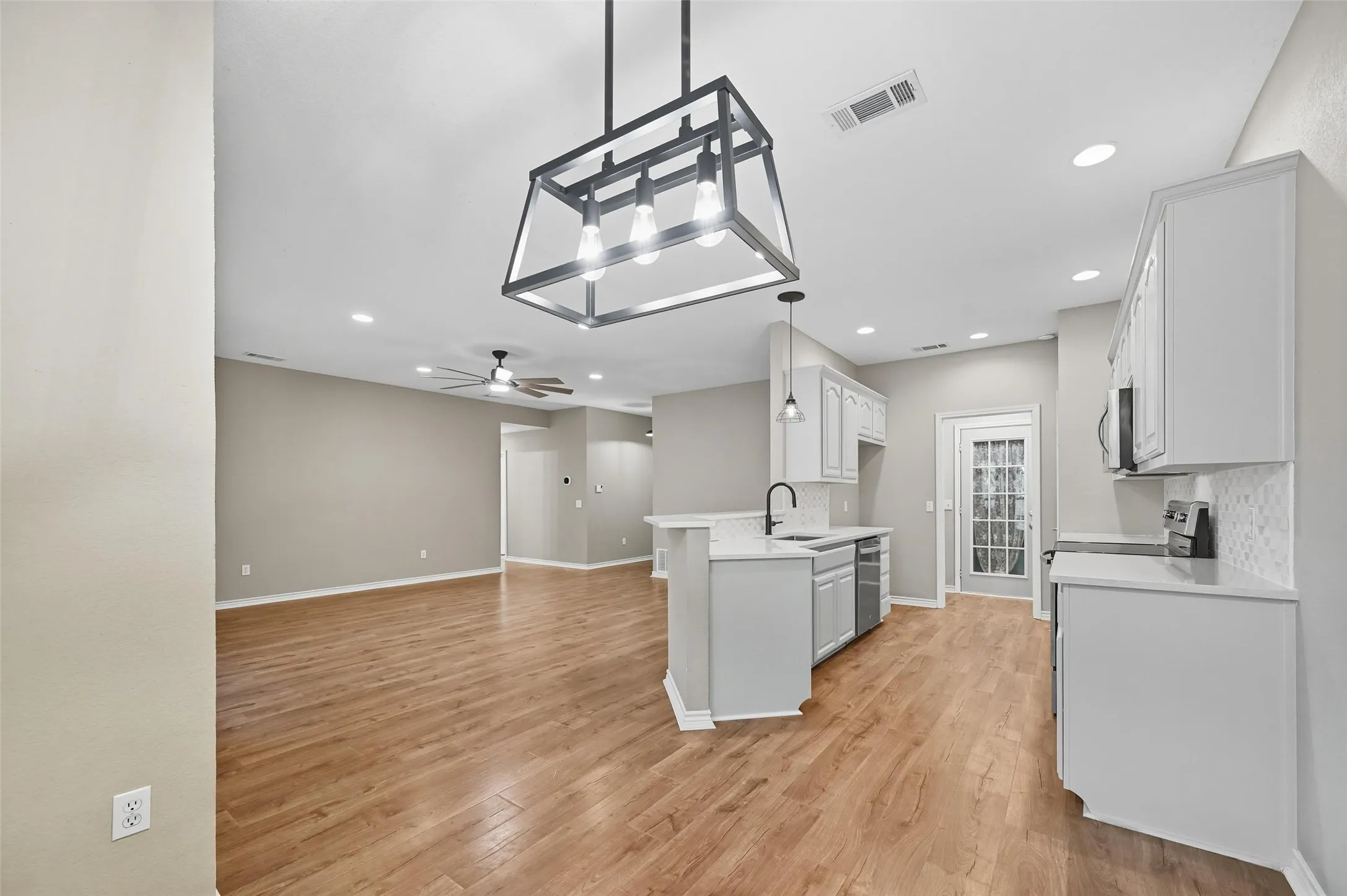 Kitchen with tasteful backsplash, decorative light fixtures, white cabinets, light wood-type flooring, and recessed lighting