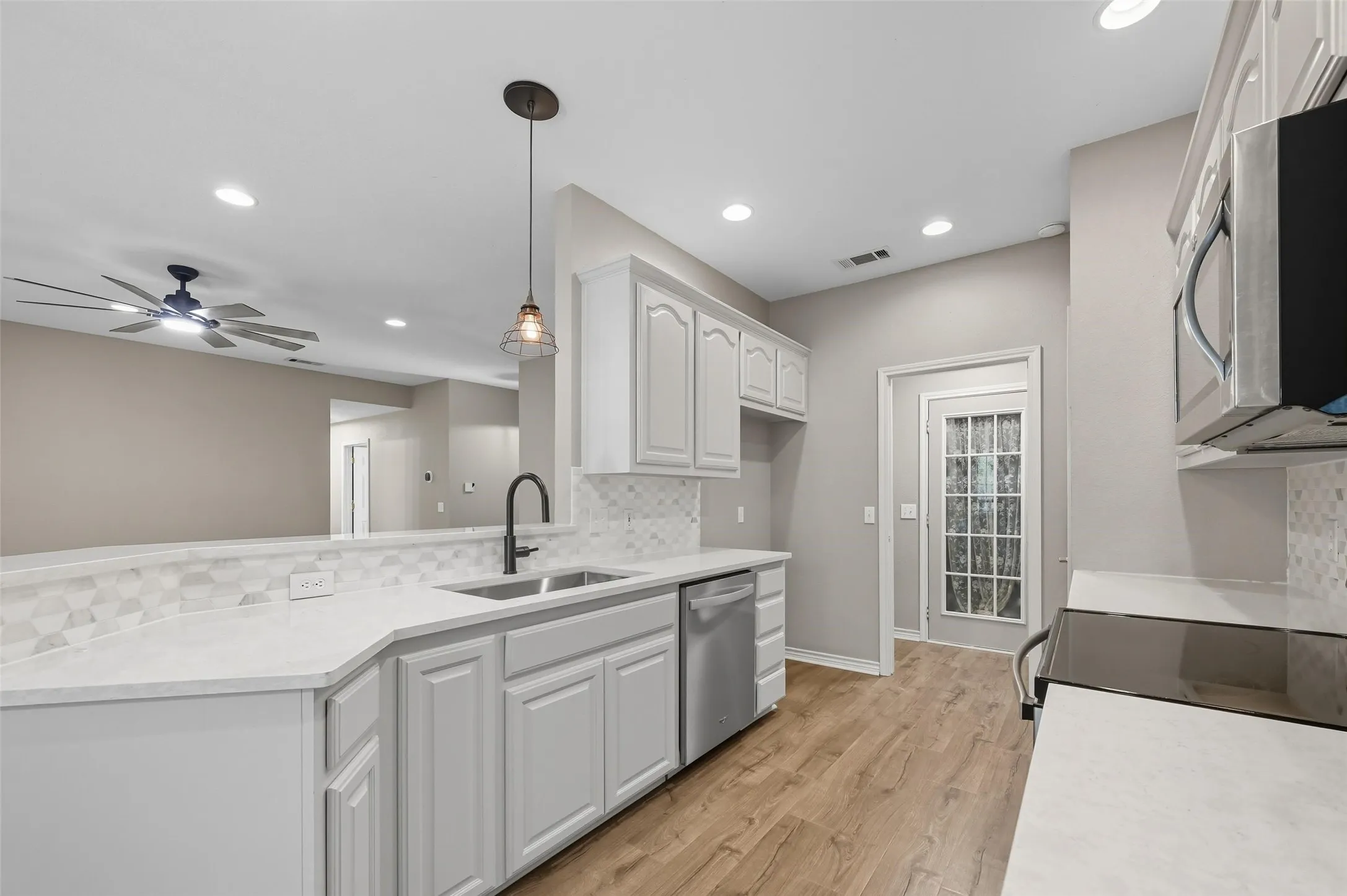 Kitchen with tasteful backsplash, light wood-style flooring, appliances with stainless steel finishes, hanging light fixtures, and white cabinets