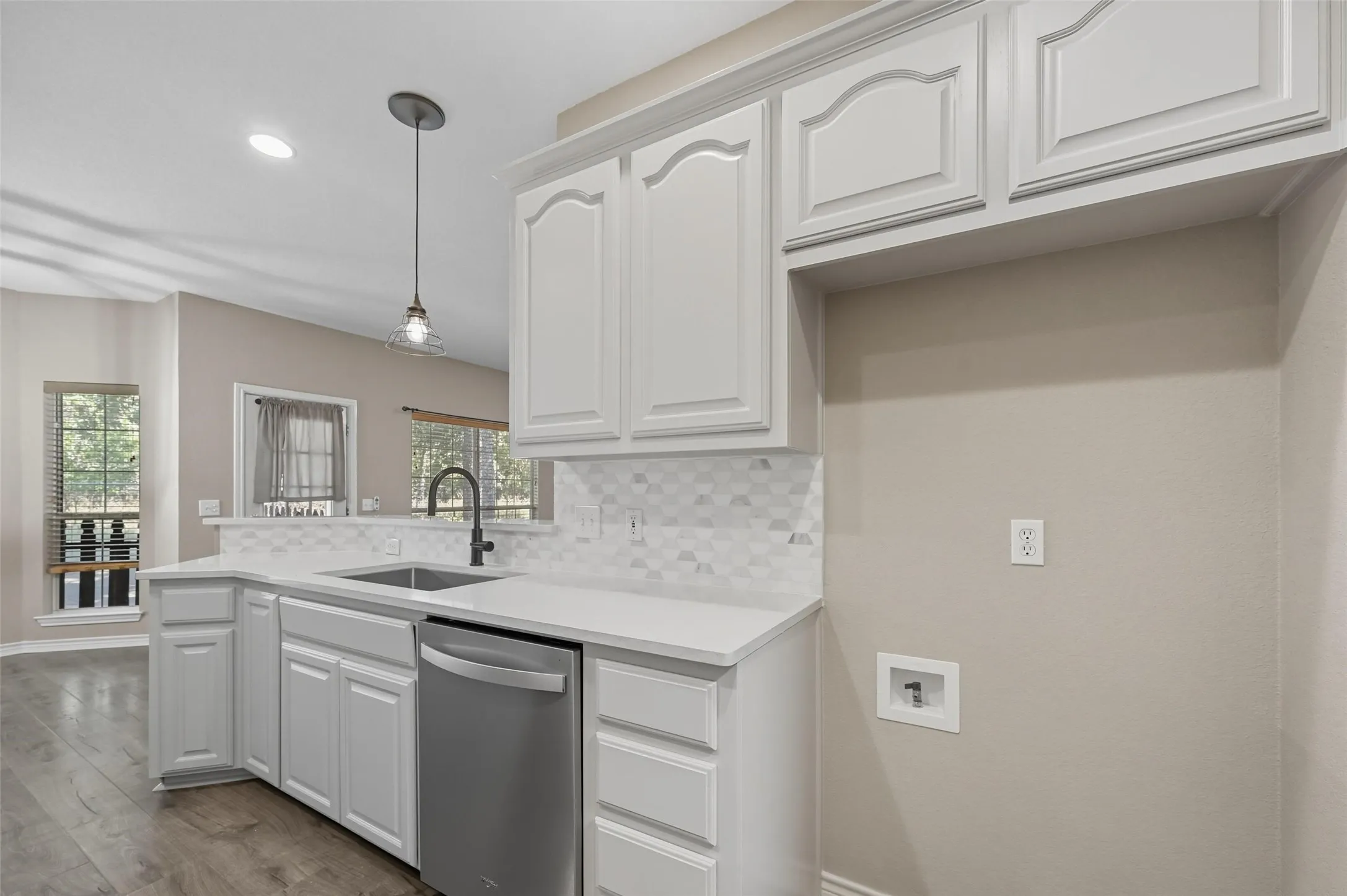 Kitchen with white cabinetry, decorative backsplash, pendant lighting, dishwasher, and a peninsula