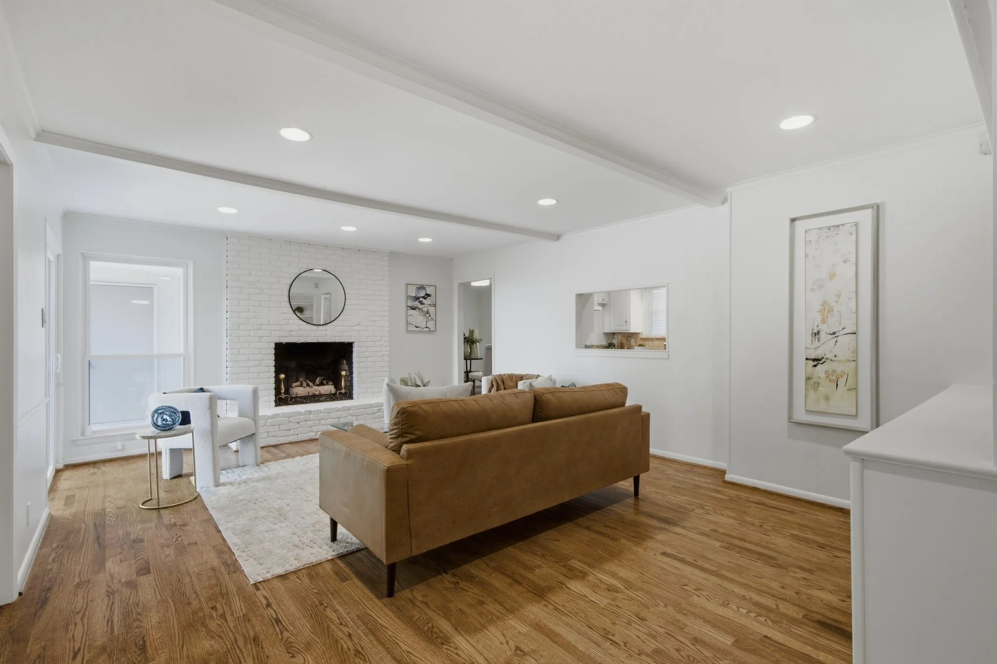 Living area featuring wood-finish flooring, a white brick fireplace, recessed lighting, and a pass-through window opening